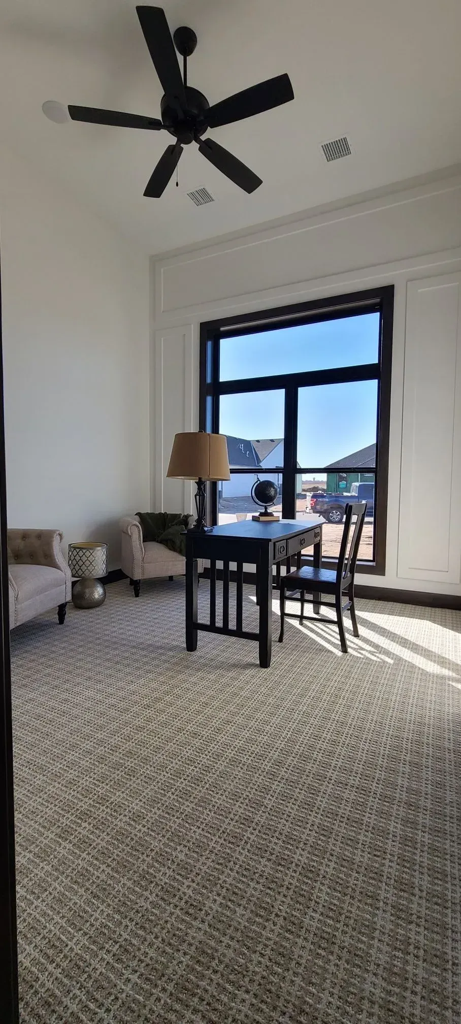 Bright living room with large window, table and chairs, couch, and ceiling fan on a patterned rug.