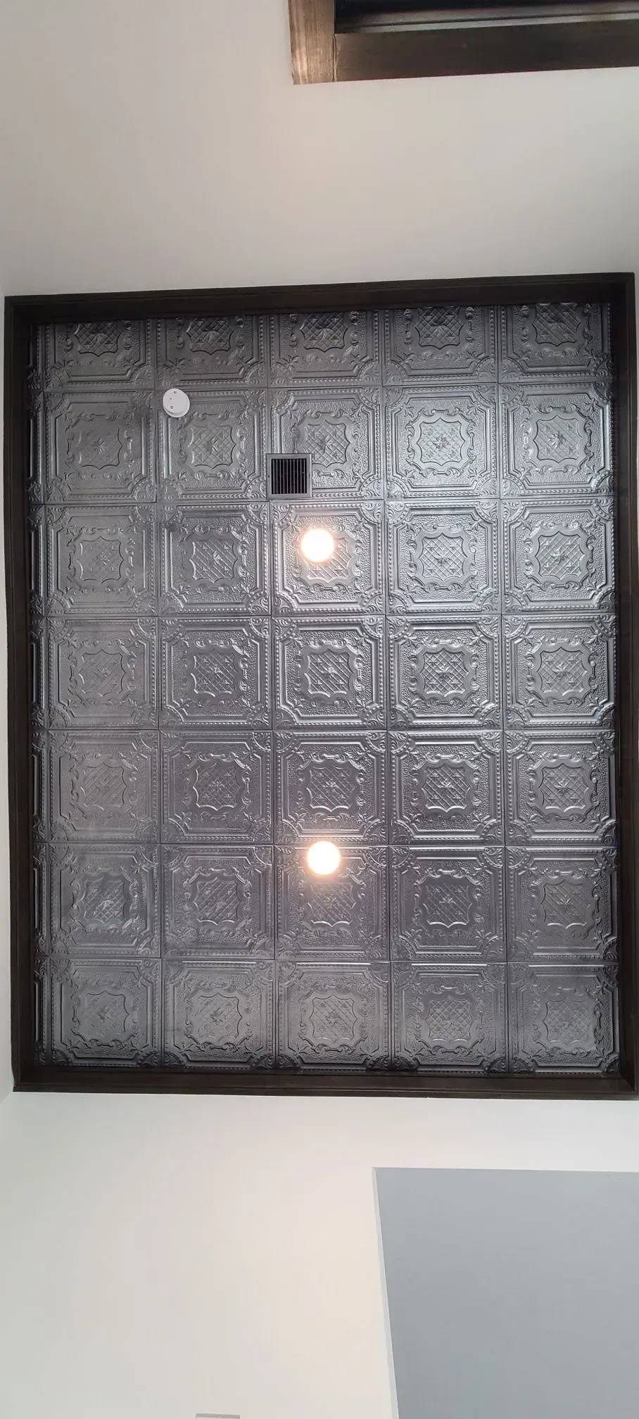 Black-framed patterned wall panel with two glowing lights on a white wall.