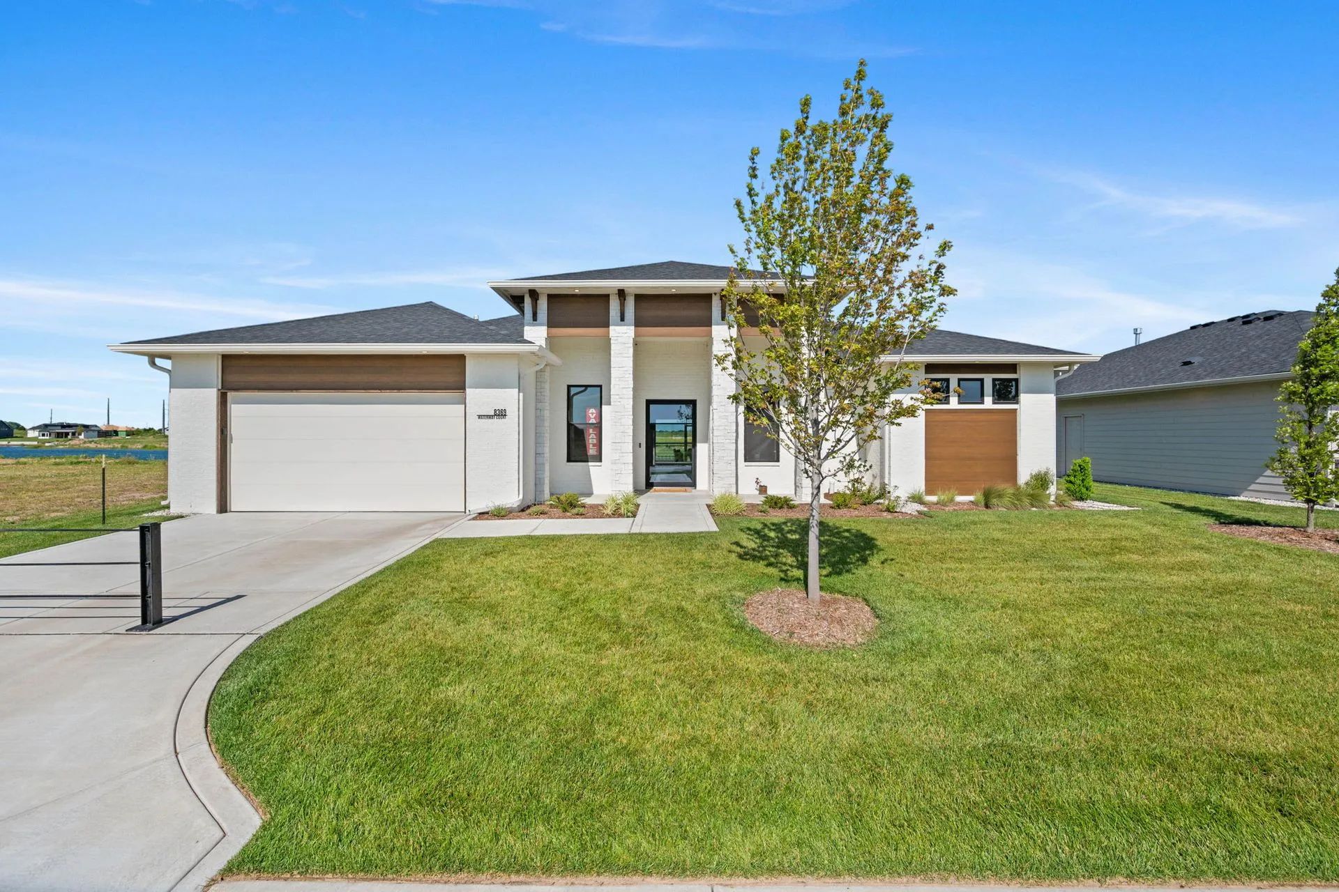 Modern single-story house with a garage, driveway, and green front lawn under a blue sky