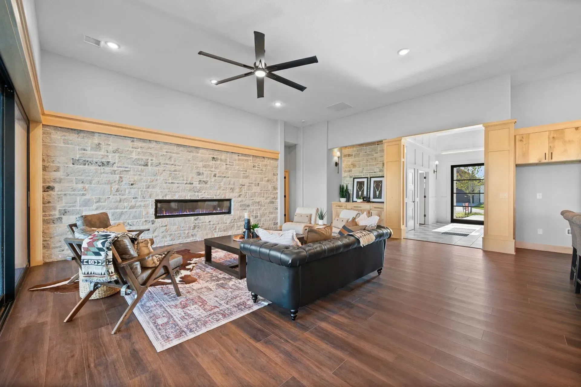 Modern living room with stone fireplace, black sofa, wood floors, and ceiling fan