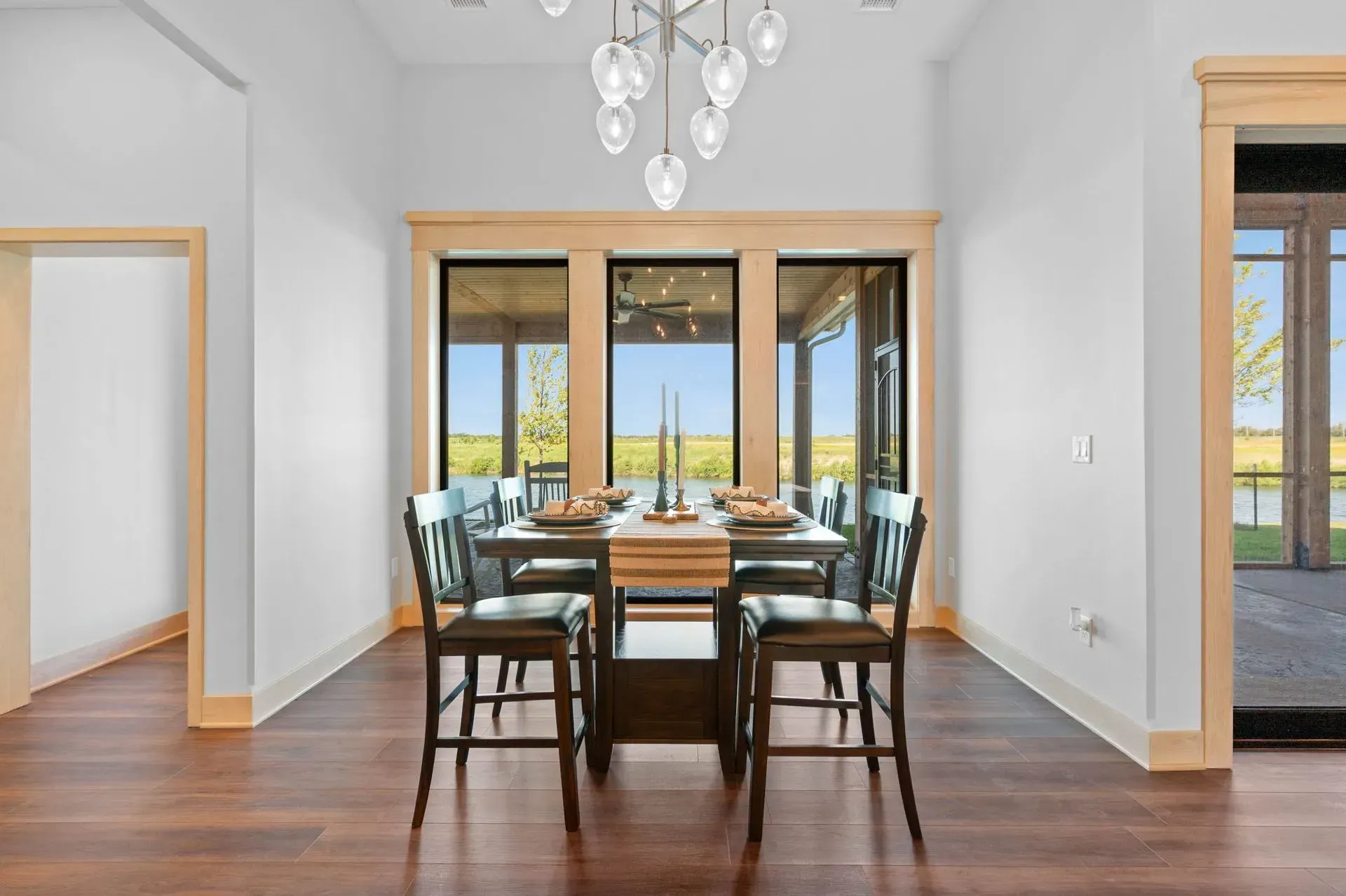 Modern dining room with dark wood table, chairs, chandelier, and large glass doors to a bright outdoor view