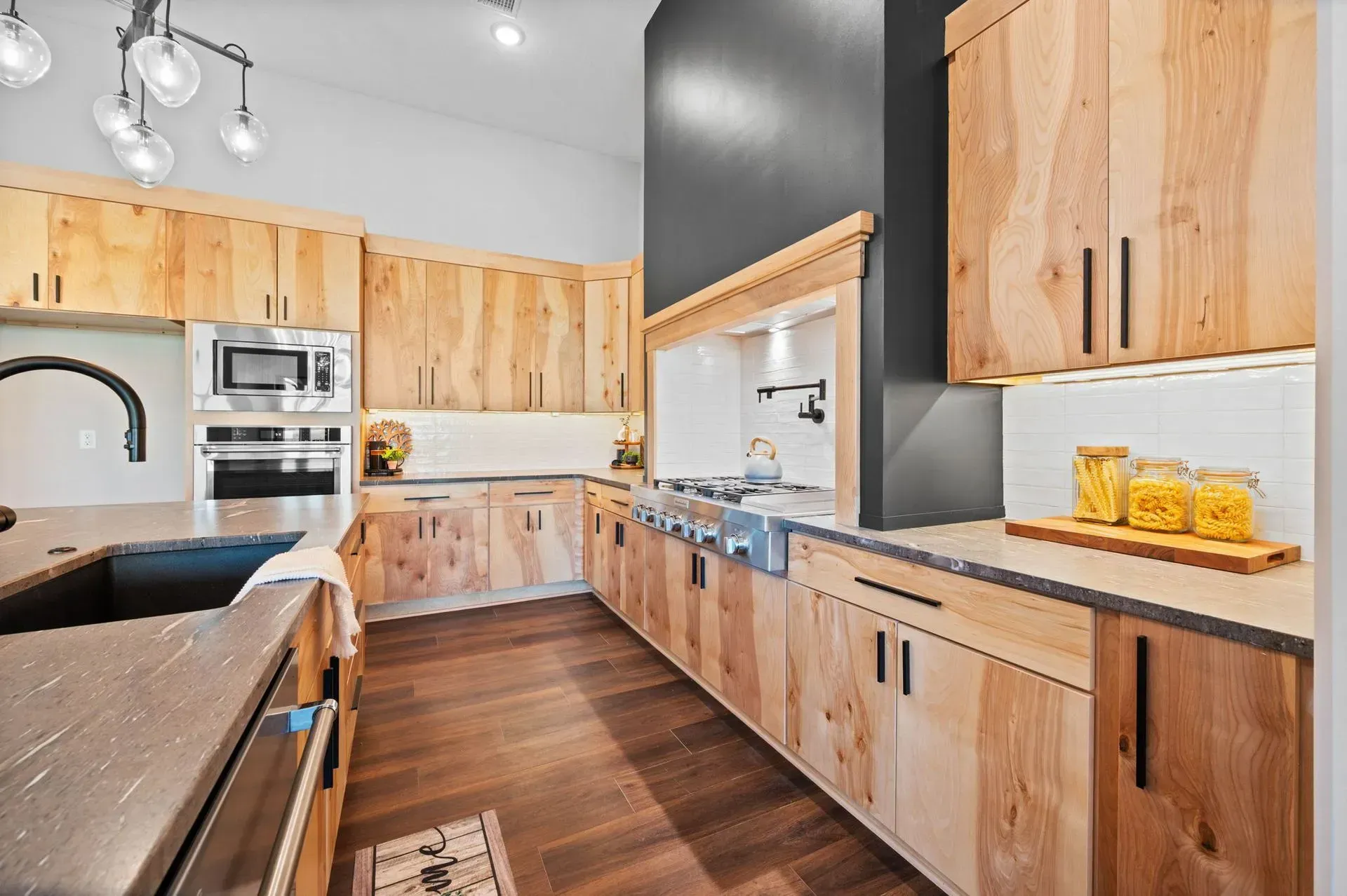 Bright modern kitchen with light wood cabinets, dark countertops, and hardwood floors.