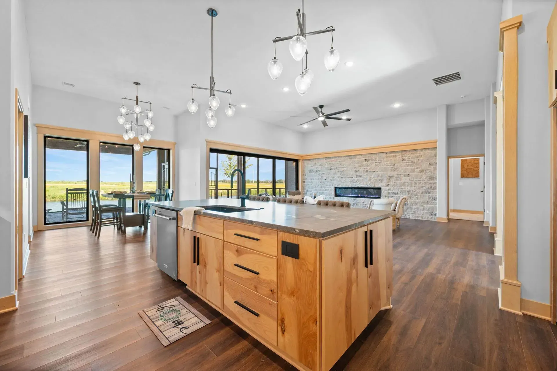 Modern kitchen with large island, wood floors, pendant lights, and sliding glass doors to a patio.