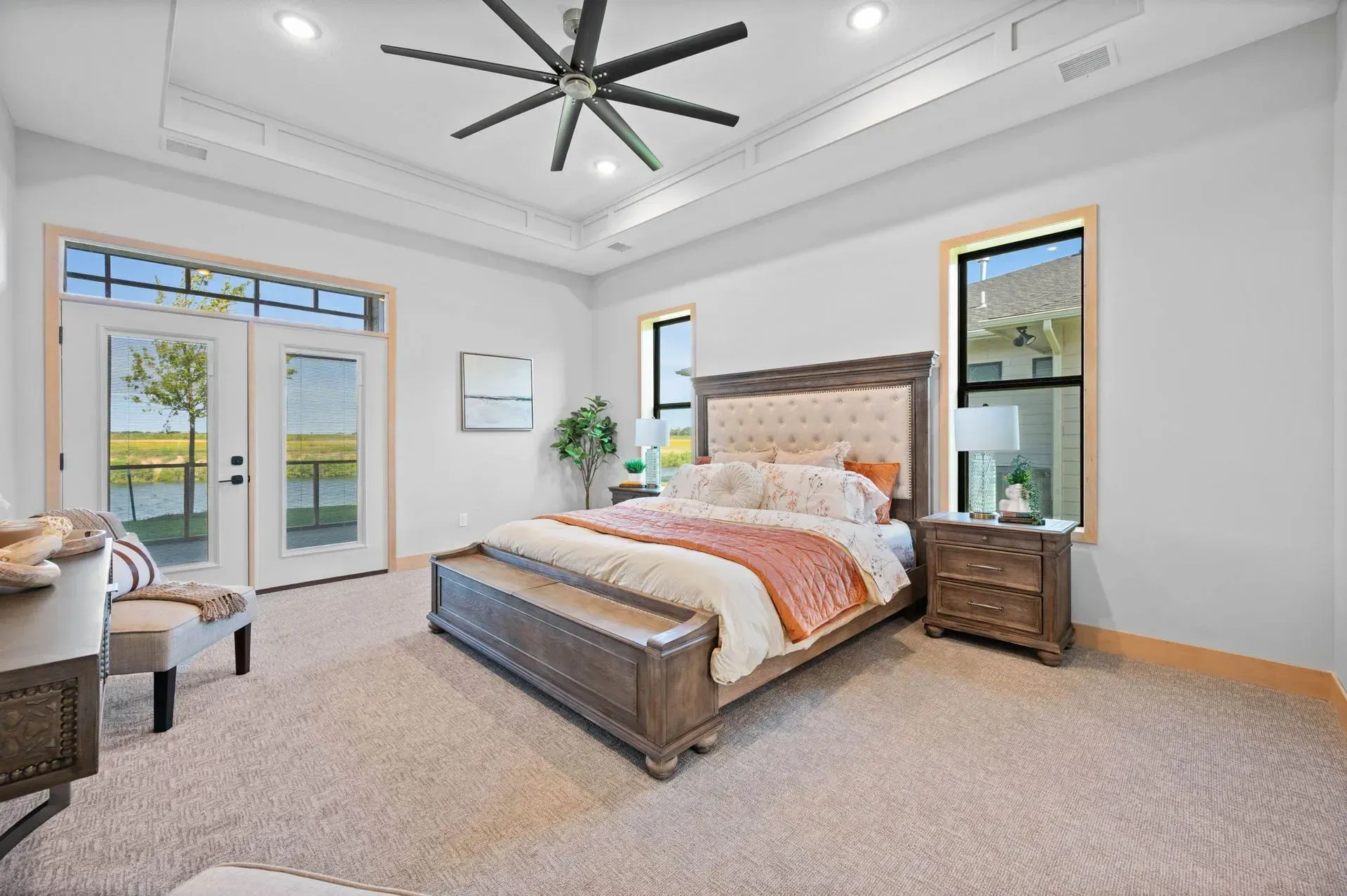 Bright modern bedroom with a wooden bed, ceiling fan, large windows, and a carpeted floor.