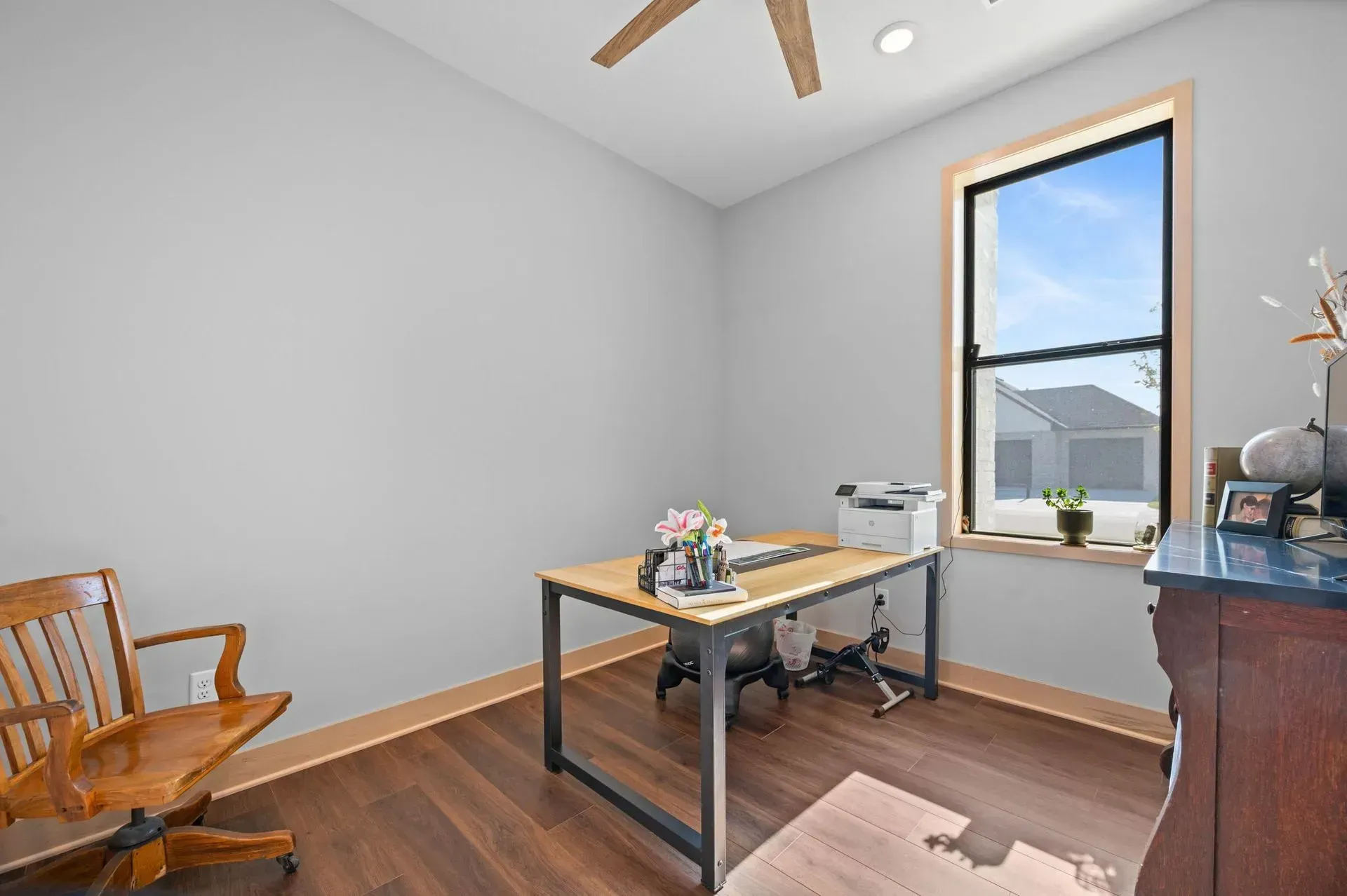 Bright home office with desk, wooden chair, window, and hardwood floors.