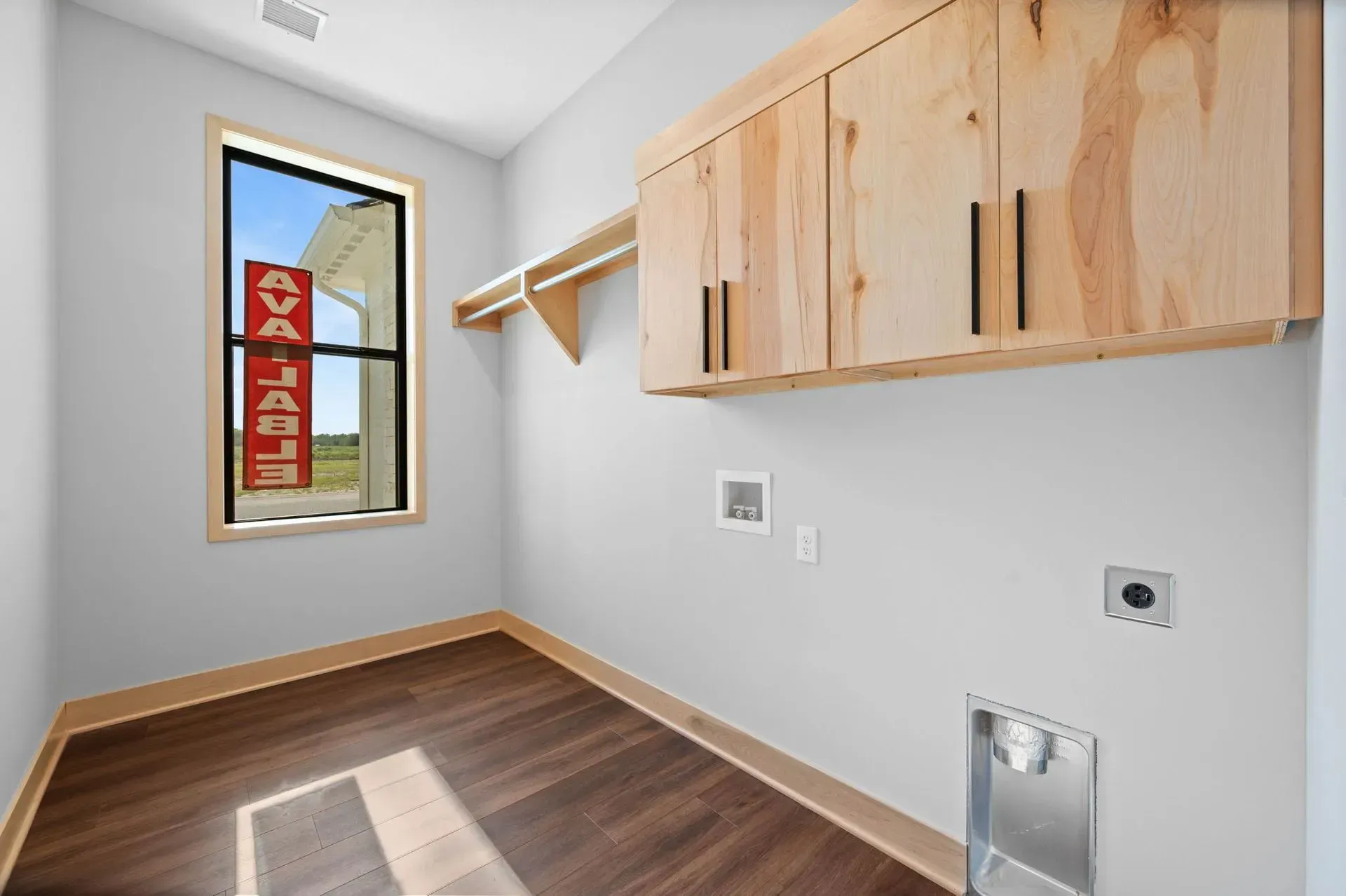 Empty laundry room with wood cabinets, wall shelf, window, and dark wood floor.