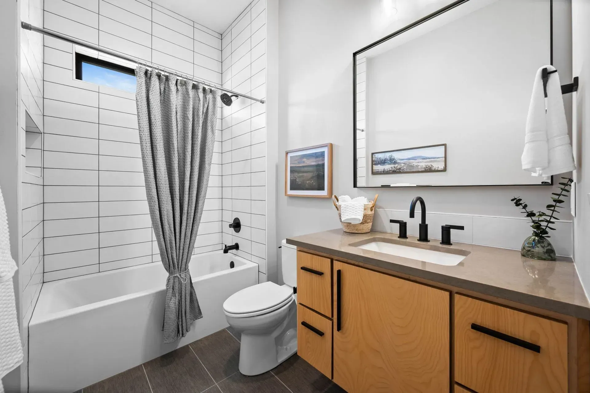 Modern bathroom with wood vanity, black fixtures, white tub, and striped shower curtain