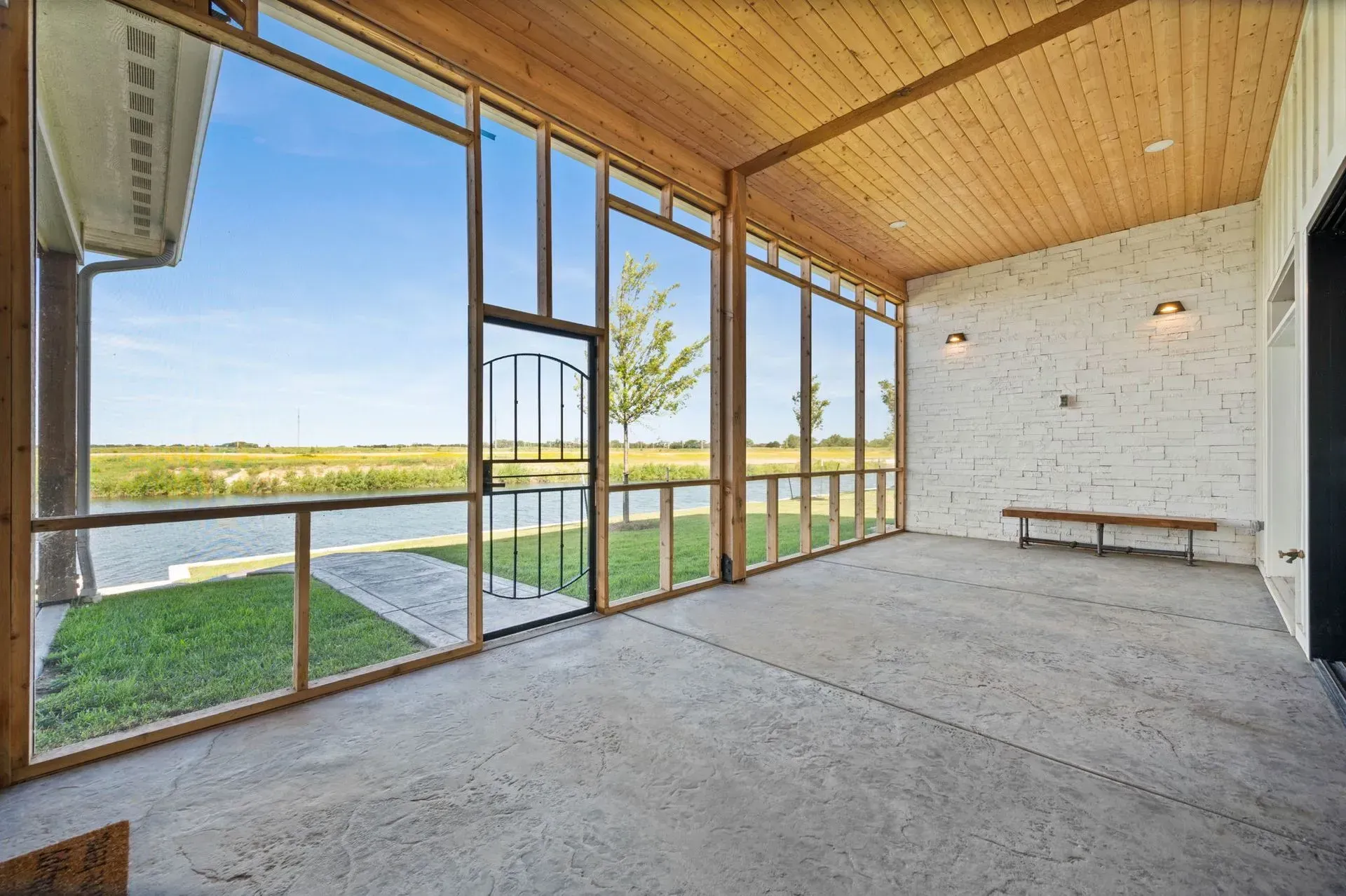 Covered patio with wood ceiling, screened glass walls, and lake view beyond a concrete floor