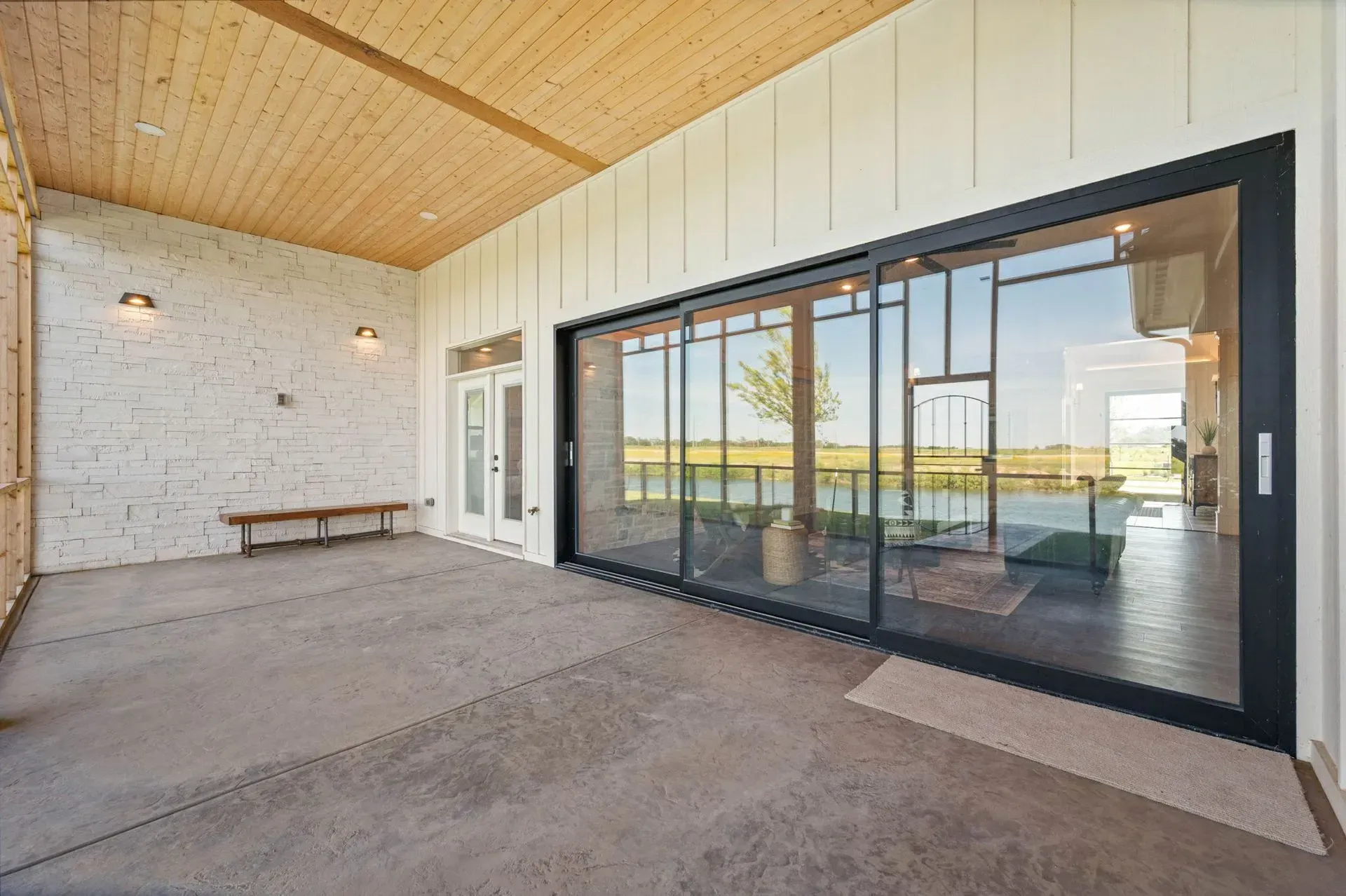 Covered patio with wood ceiling, white brick wall, bench, and large sliding glass doors