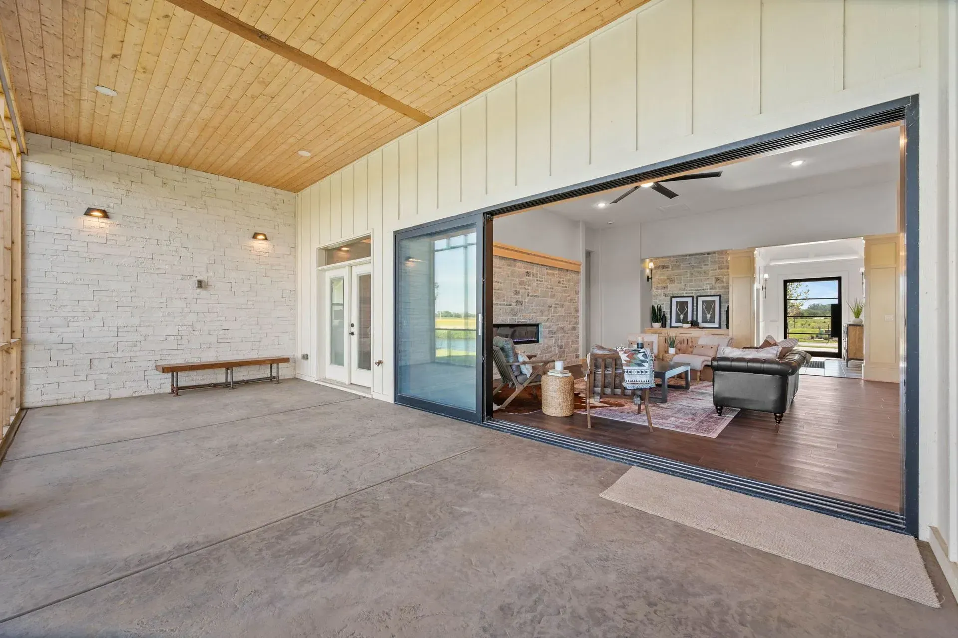 Covered patio with wood ceiling, concrete floor, and large sliding glass doors to a living room.