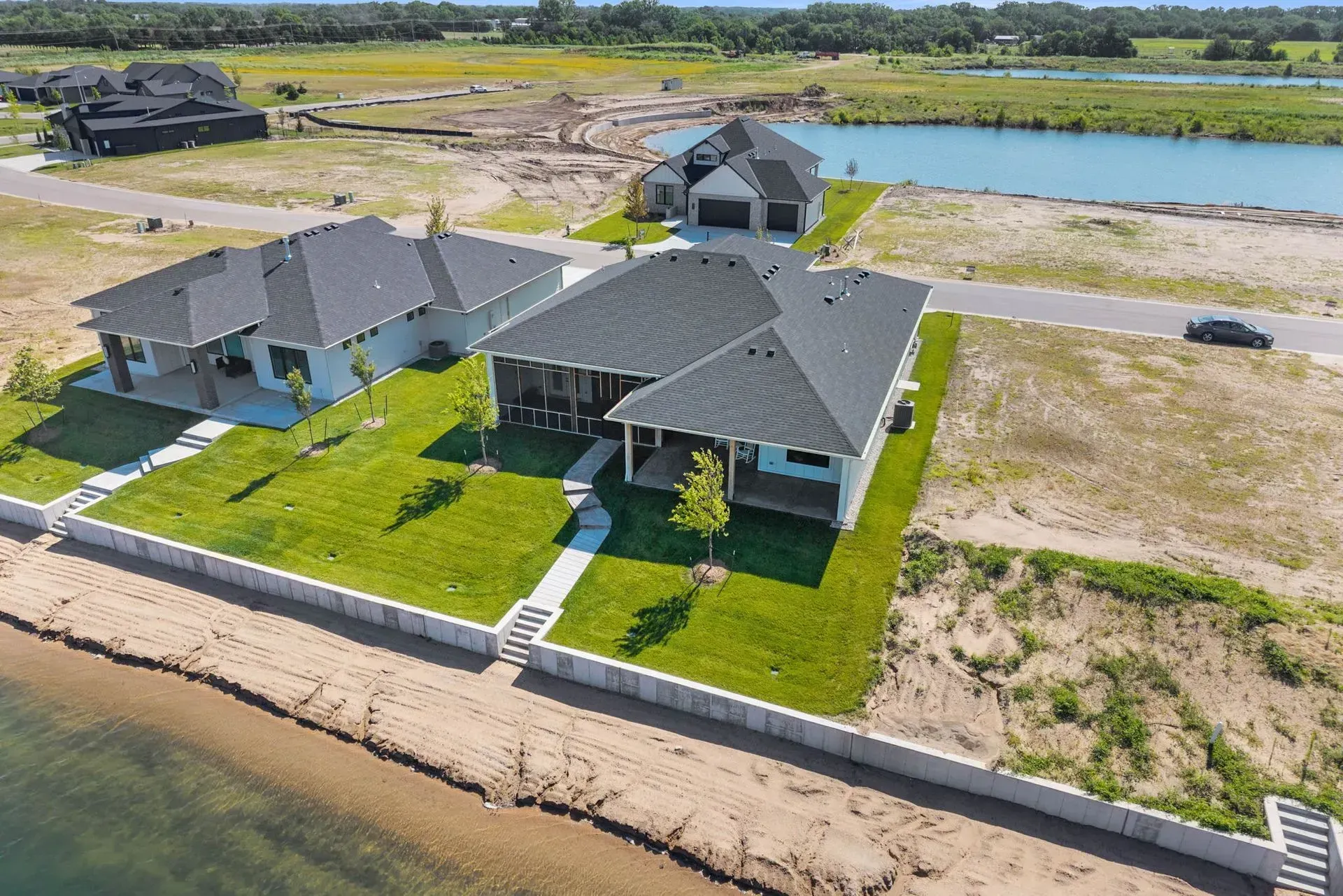 Modern waterfront house with green lawn, gray roof, and a small dock beside the water