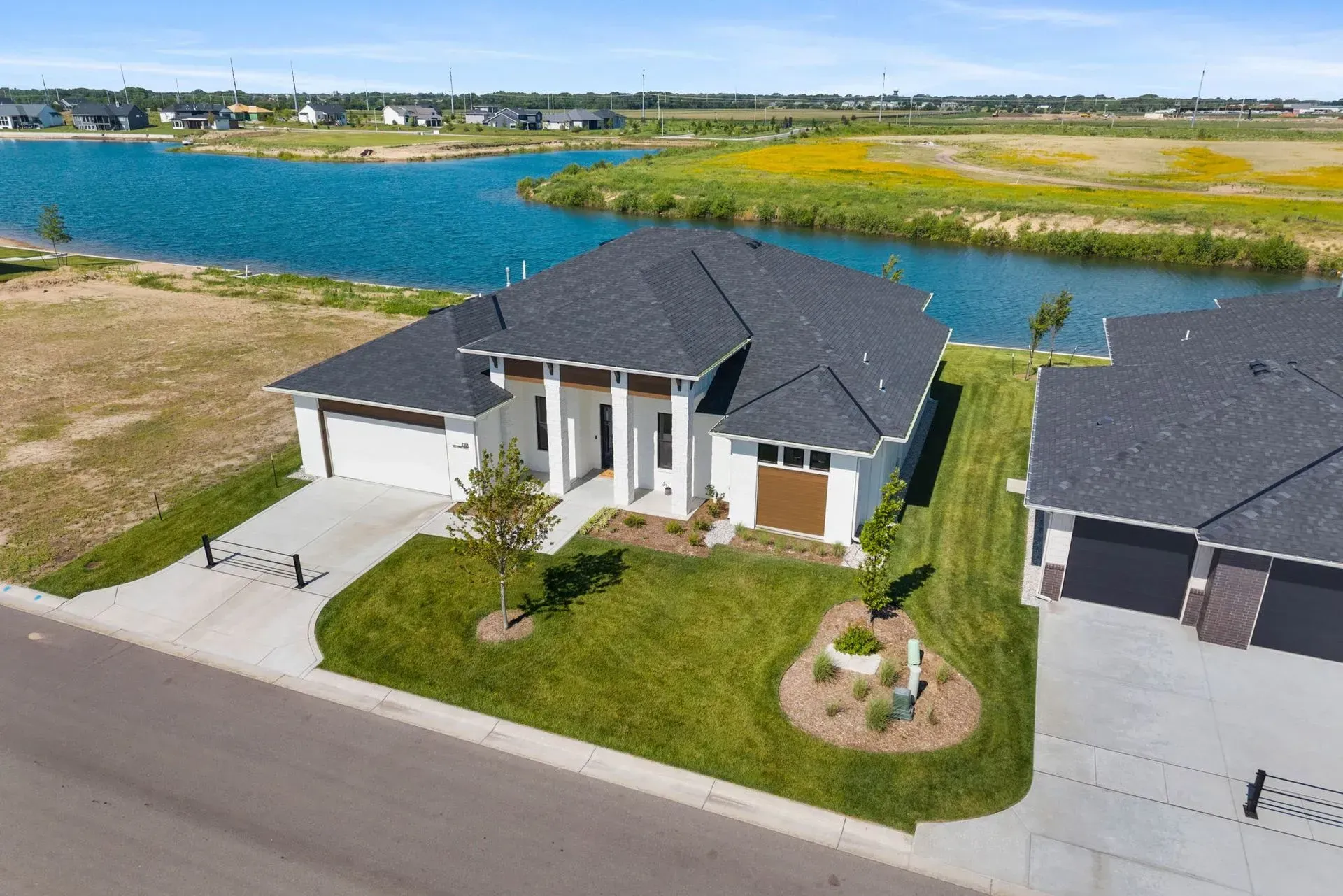 Aerial view of a modern suburban house beside a blue lake, with a driveway and green lawn.