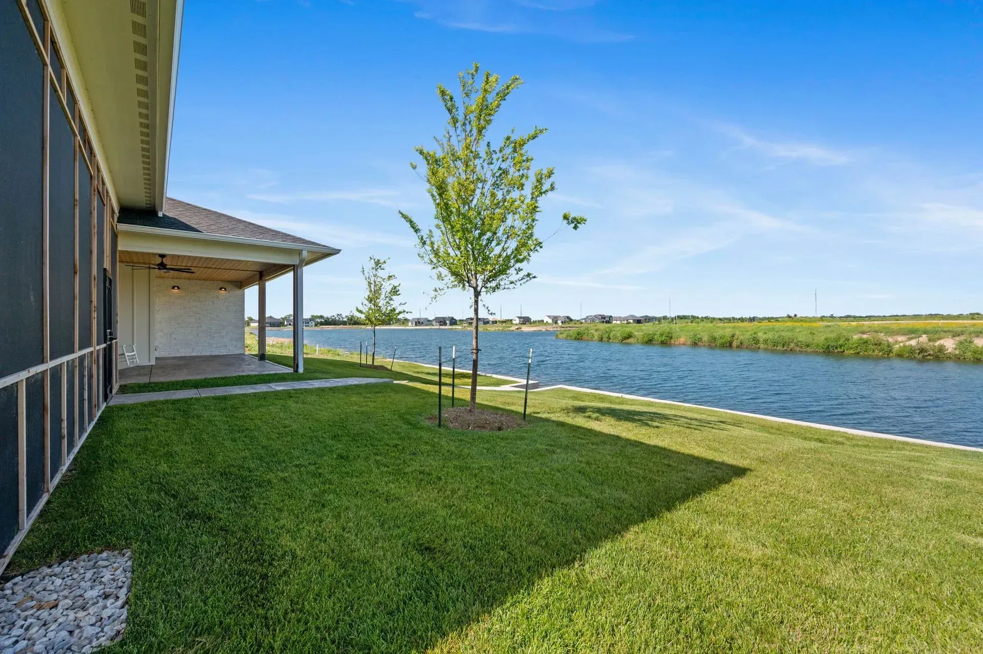 Modern house lawn beside a canal, with a young tree under a blue sky