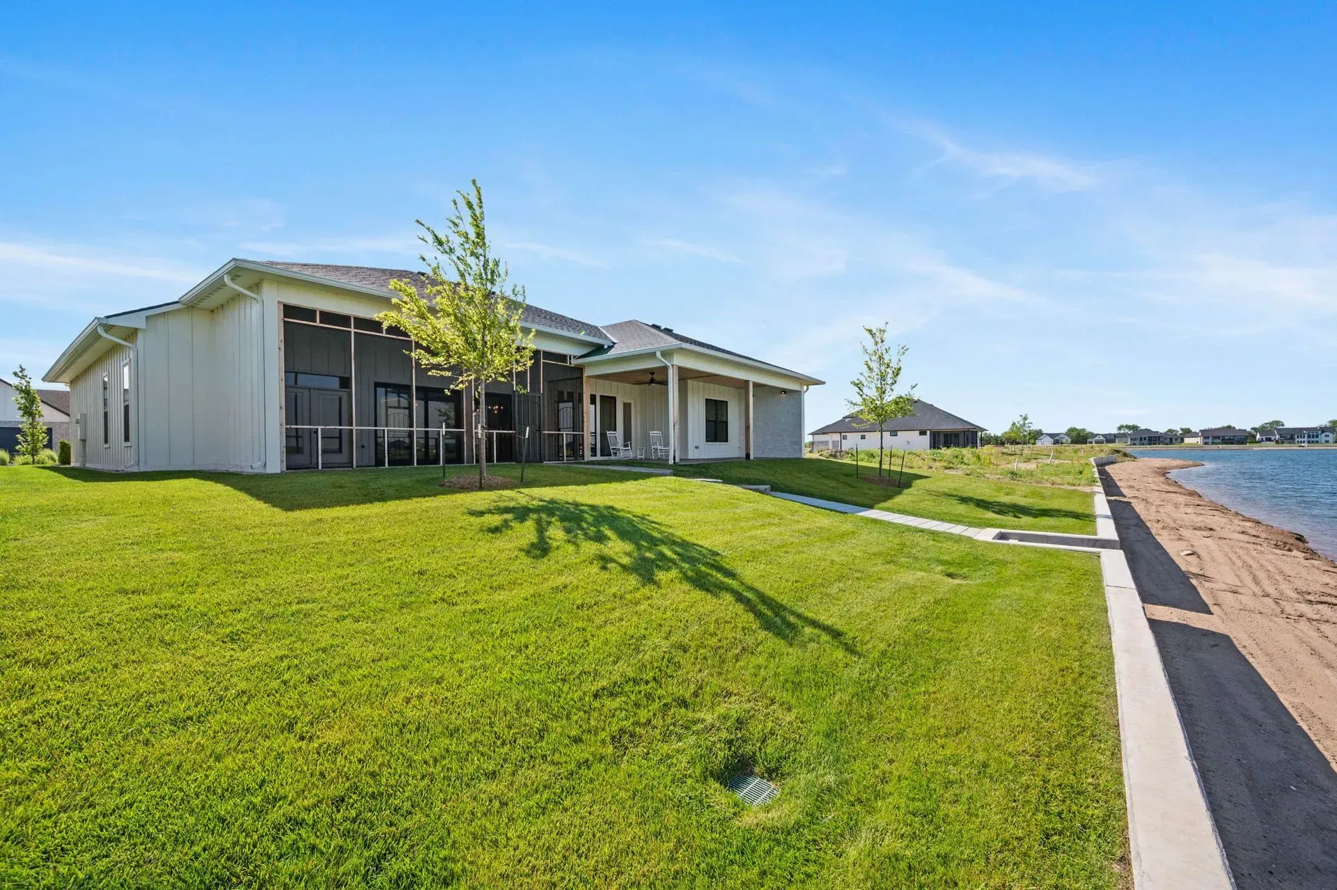 Modern single-story house with large windows, bright green lawn, and clear blue sky on a sunny day