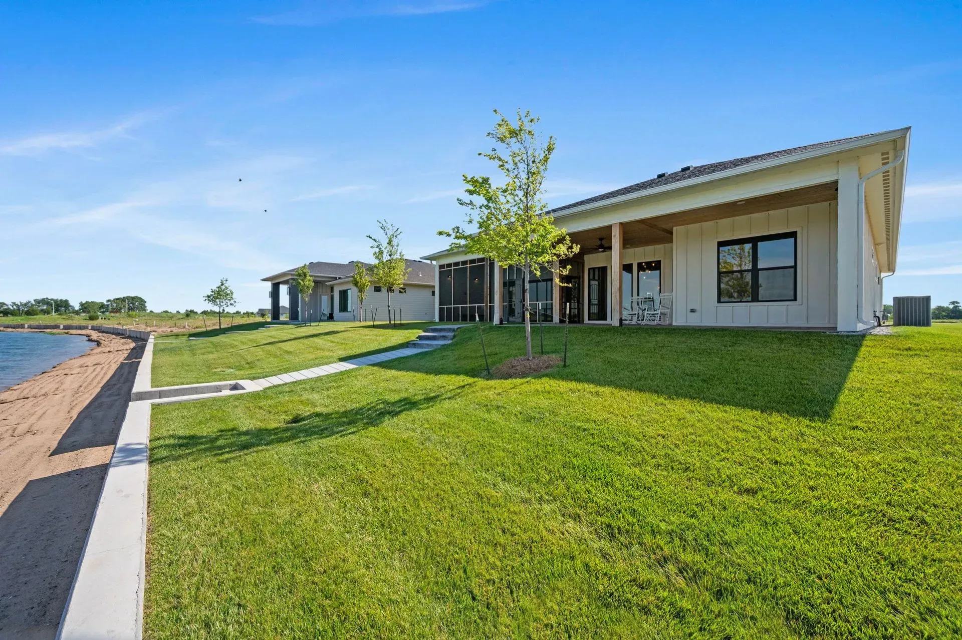 Modern single-story house with a green lawn, paved driveway, and blue sky