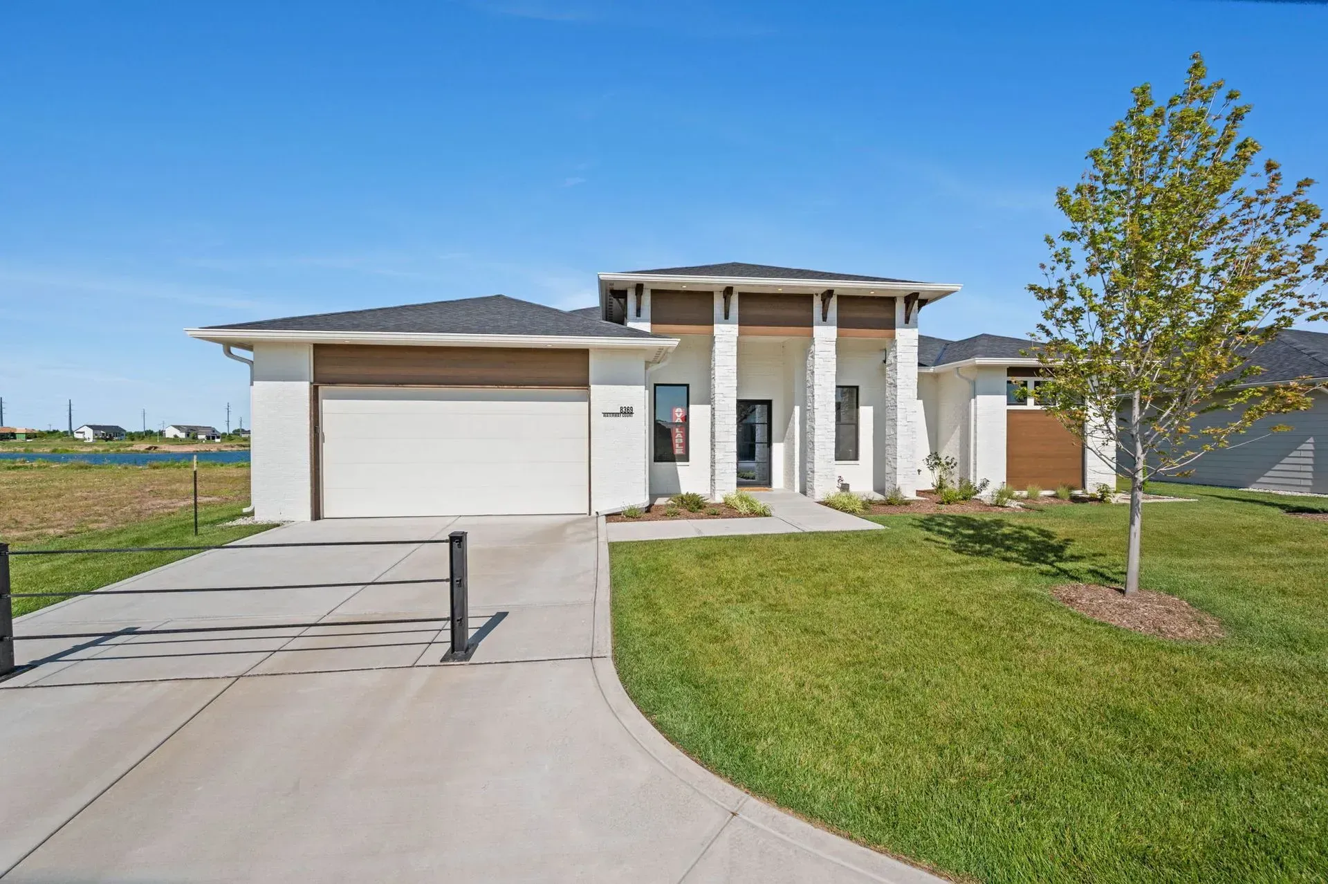 Modern single-story house with garage, front porch columns, and a curved driveway on a sunny day