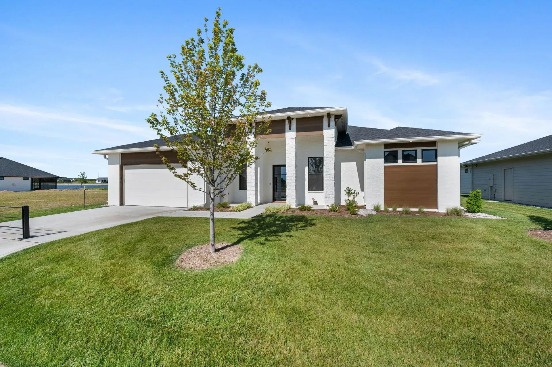 Modern single-story suburban house with a two-car garage, white columns, and a large green lawn