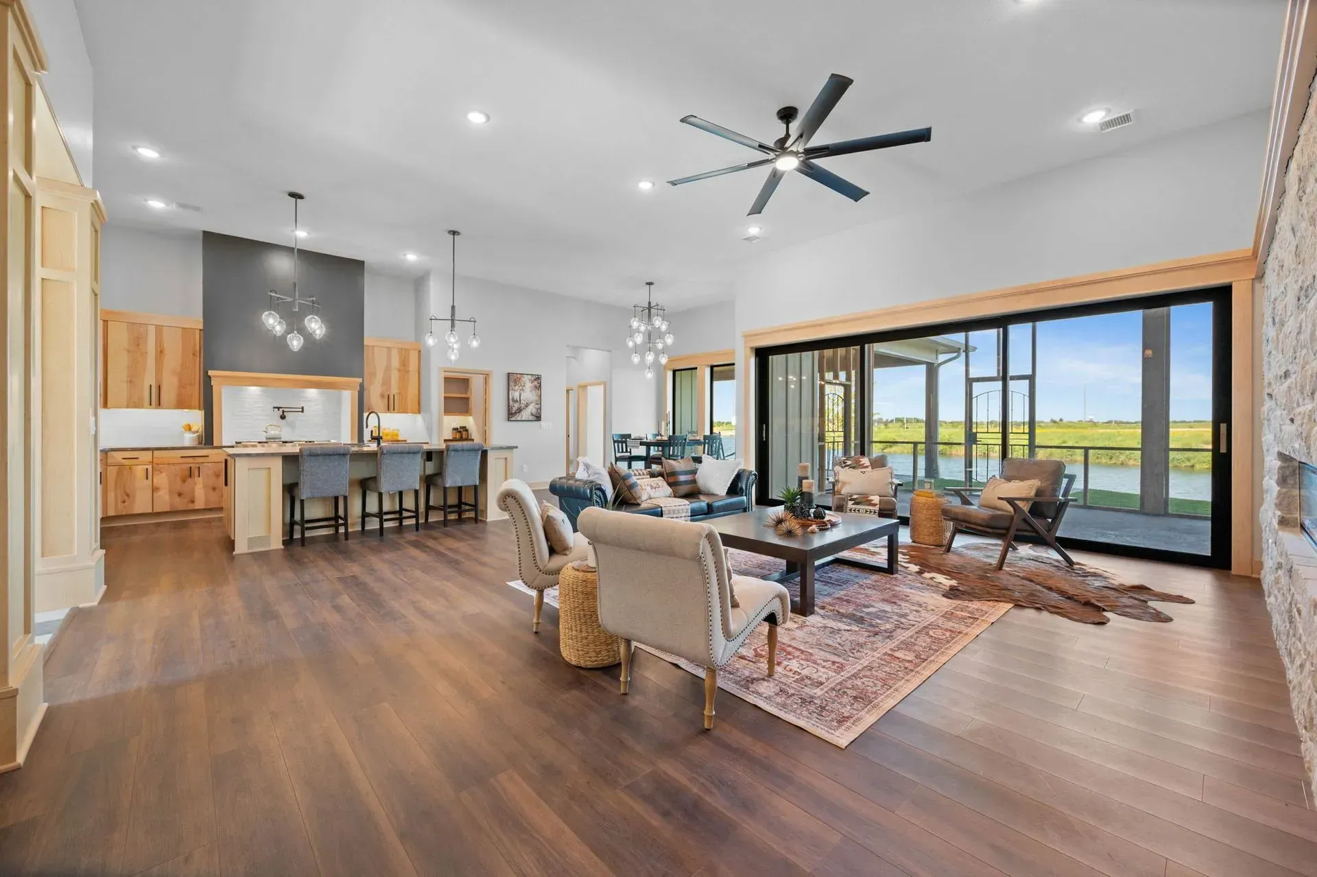 Bright open-concept living room with kitchen, modern ceiling fan, and large sliding glass doors to a patio.