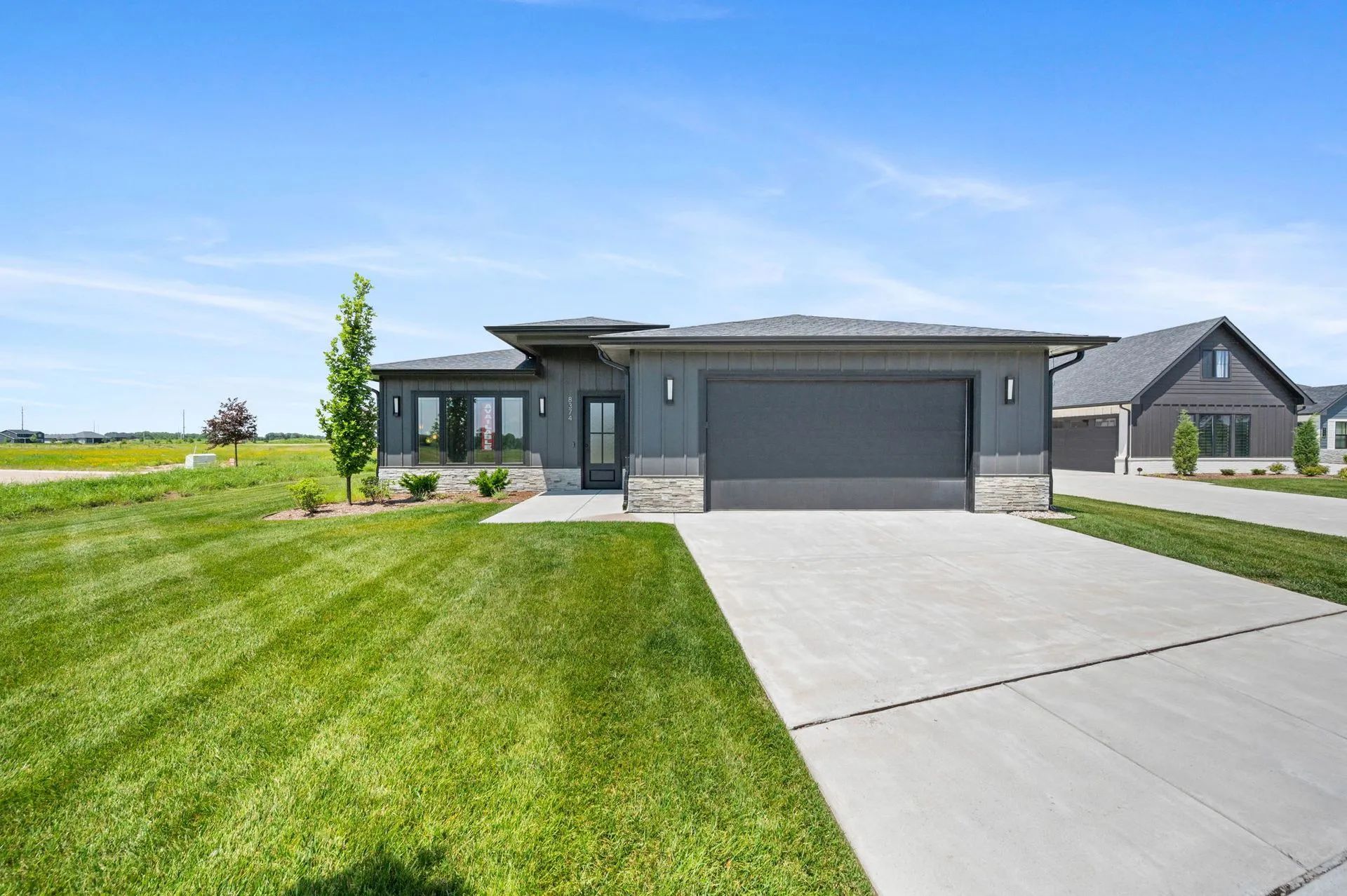 Modern gray single-story house with a two-car garage, driveway, and green lawn under a blue sky