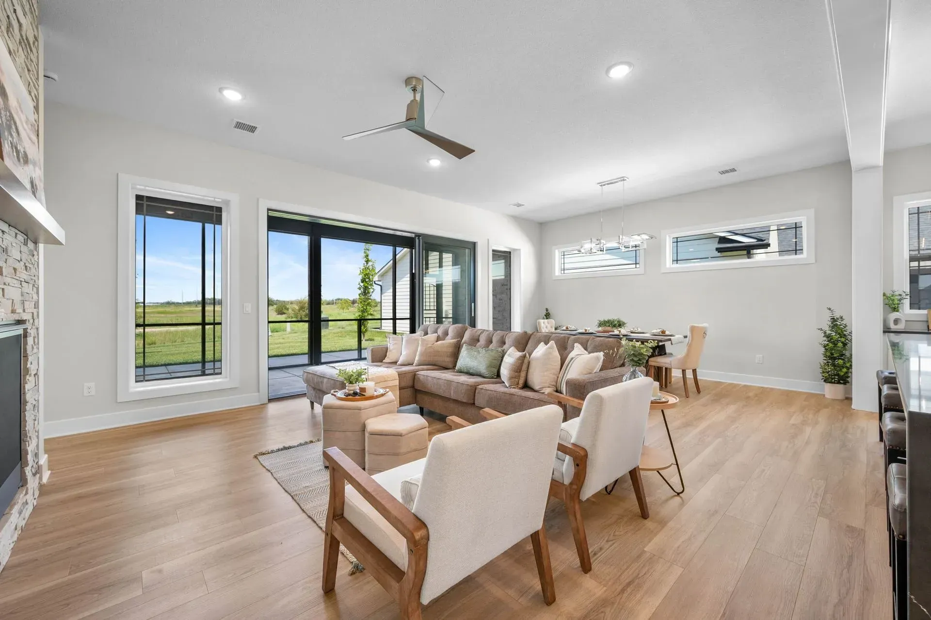 Bright modern living room with beige sofas, wood floors, large windows, and a dining area