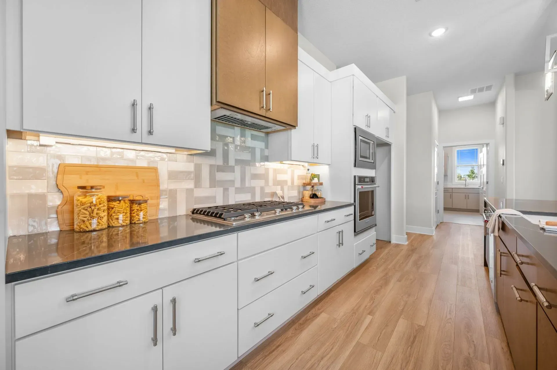 Bright modern galley kitchen with white cabinets, wood accents, and hardwood floors