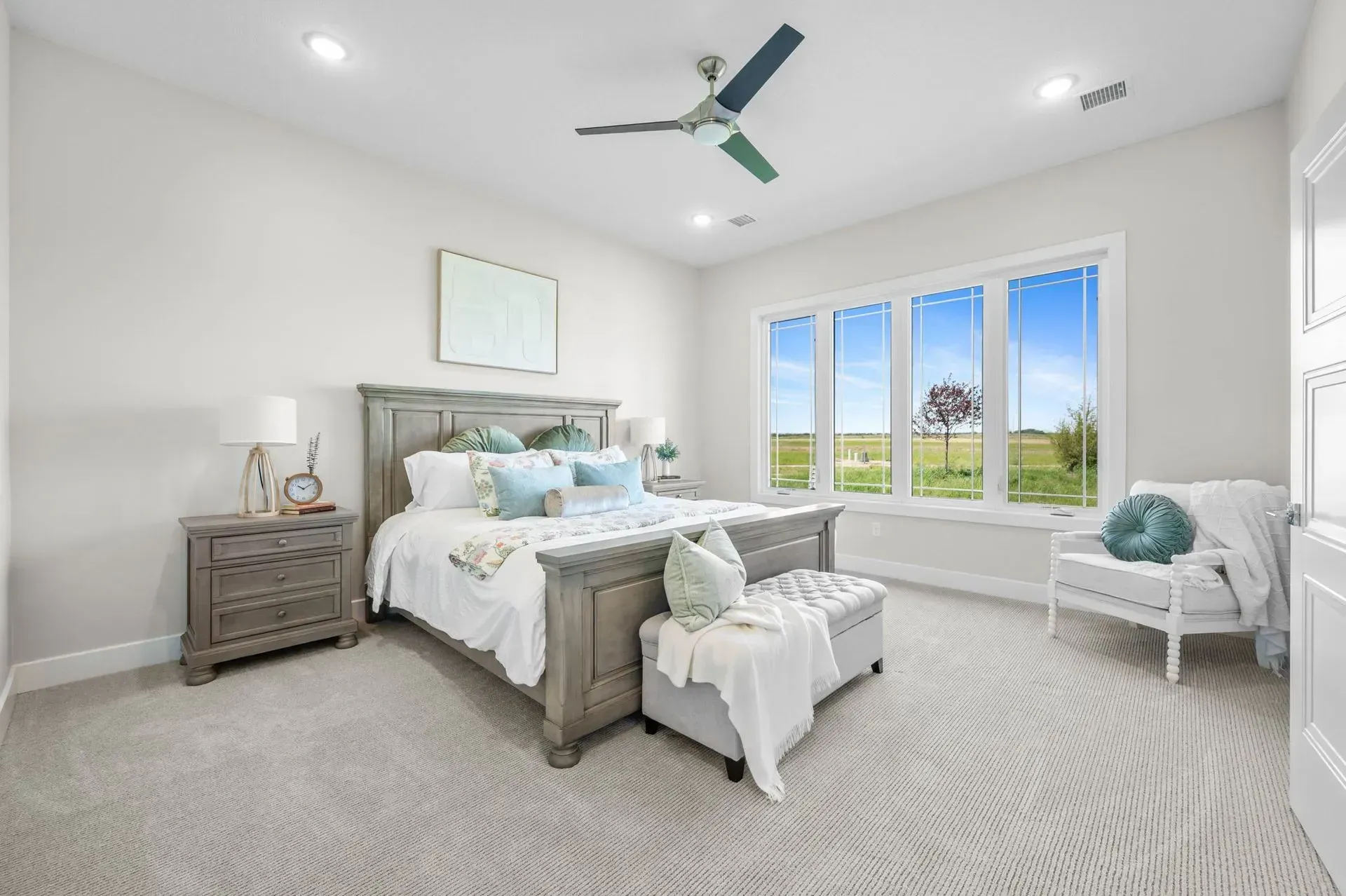 Bright white bedroom with twin beds, gray carpet, and large windows overlooking a green yard