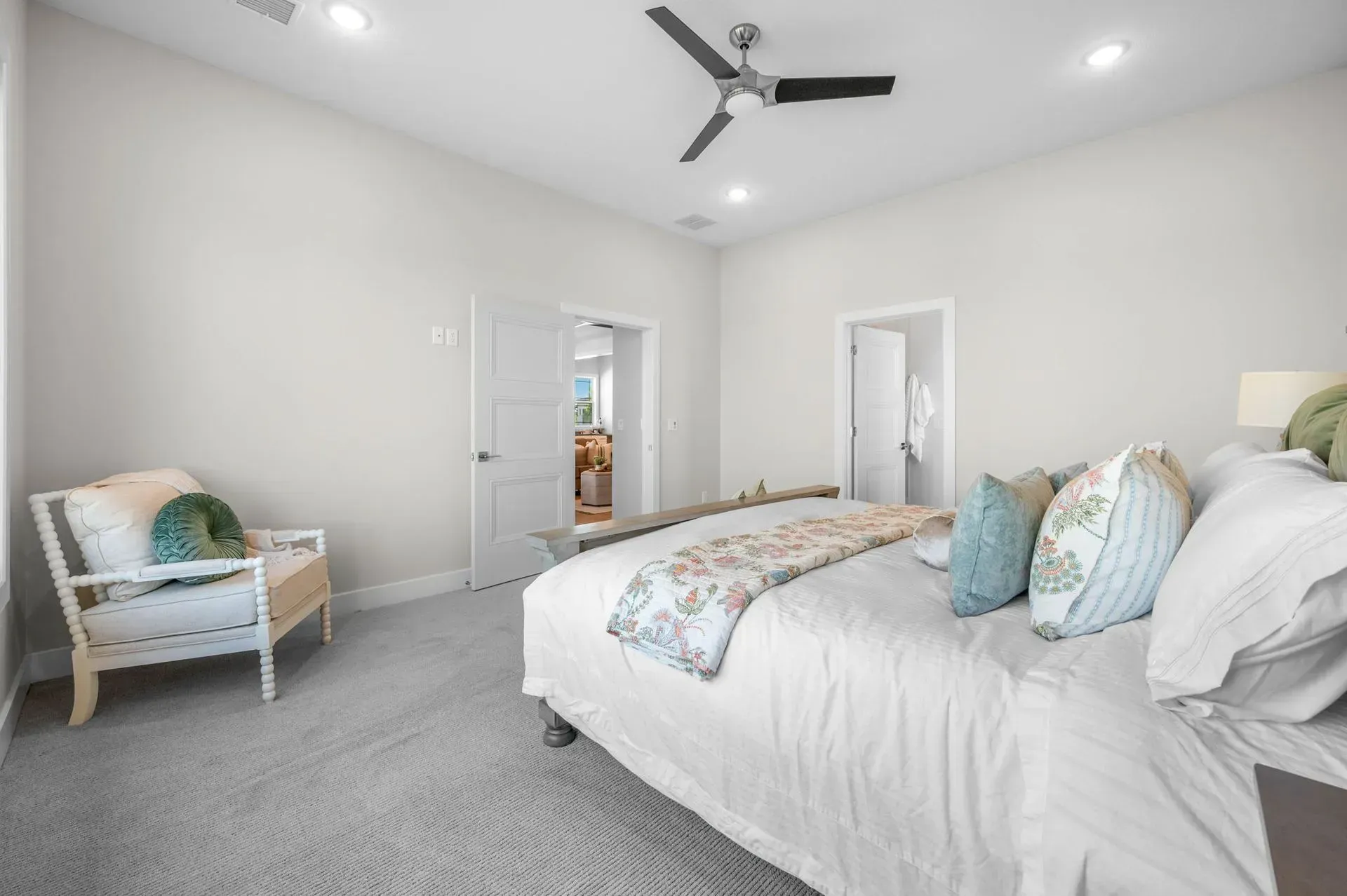 Bright white bedroom with gray carpet, a large bed, chair, ceiling fan, and open doors.