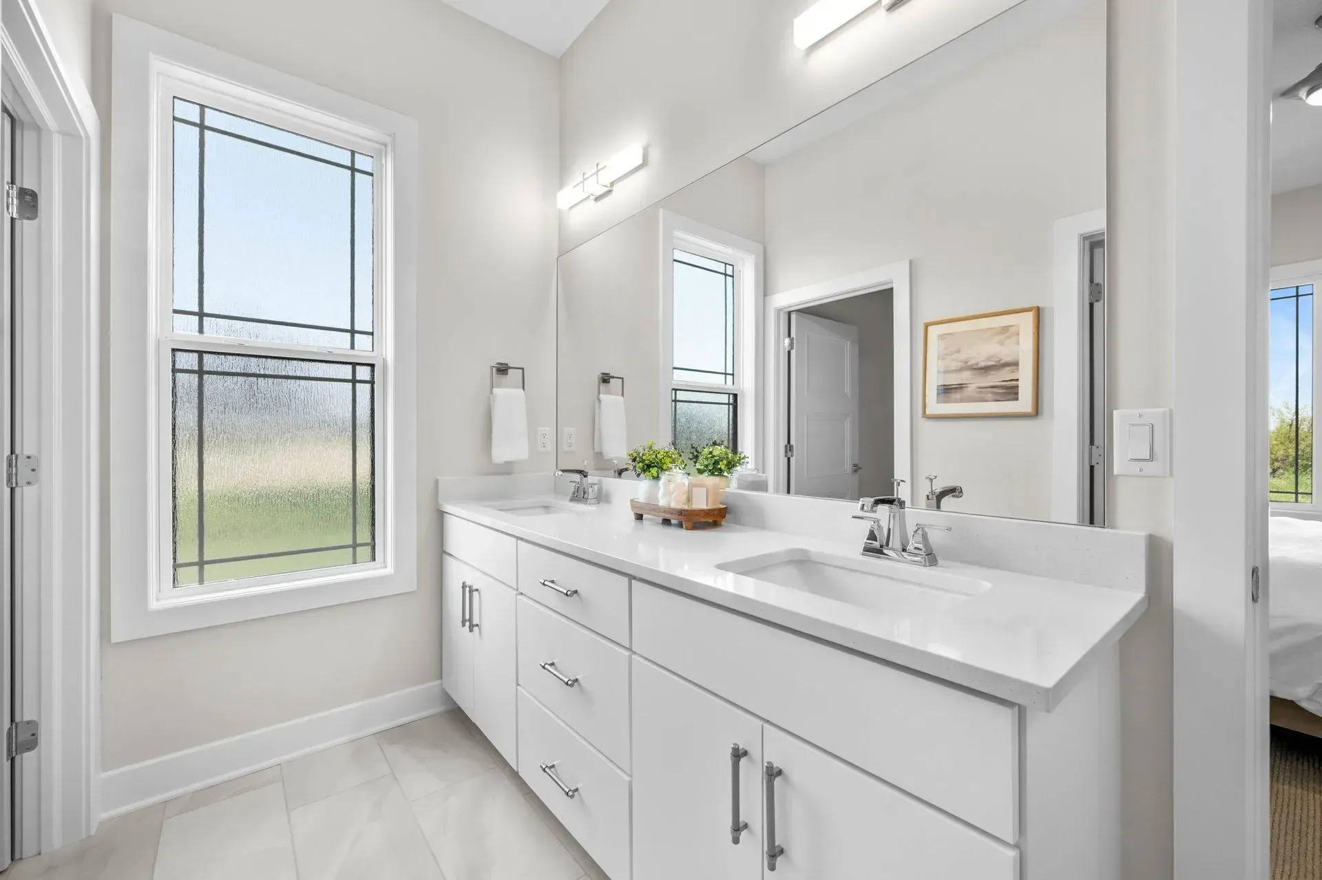 Bright modern bathroom with a double vanity, large mirror, and window view of a green yard