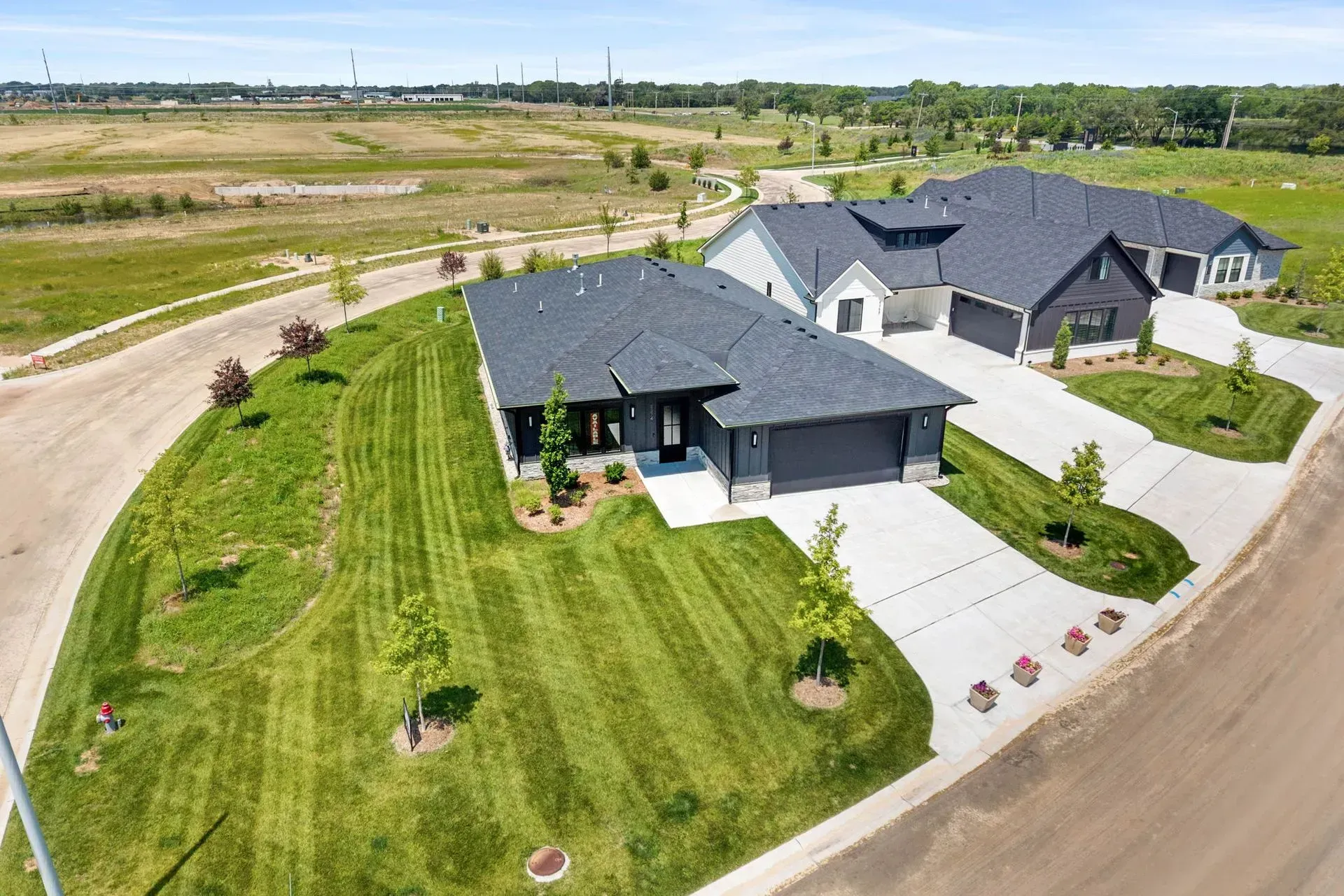Aerial view of a modern suburban house with a large lawn and driveway in a rural neighborhood.