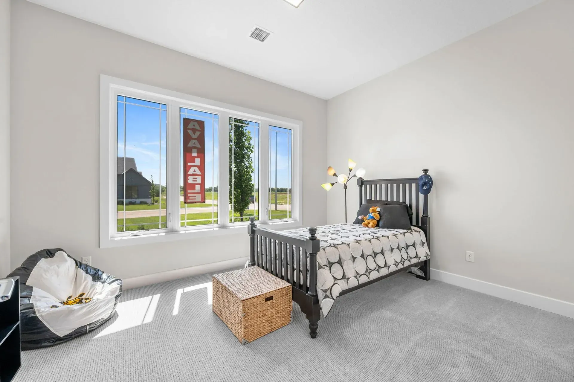 Bright bedroom with a gray bed, large window, and carpeted floor in a modern home.