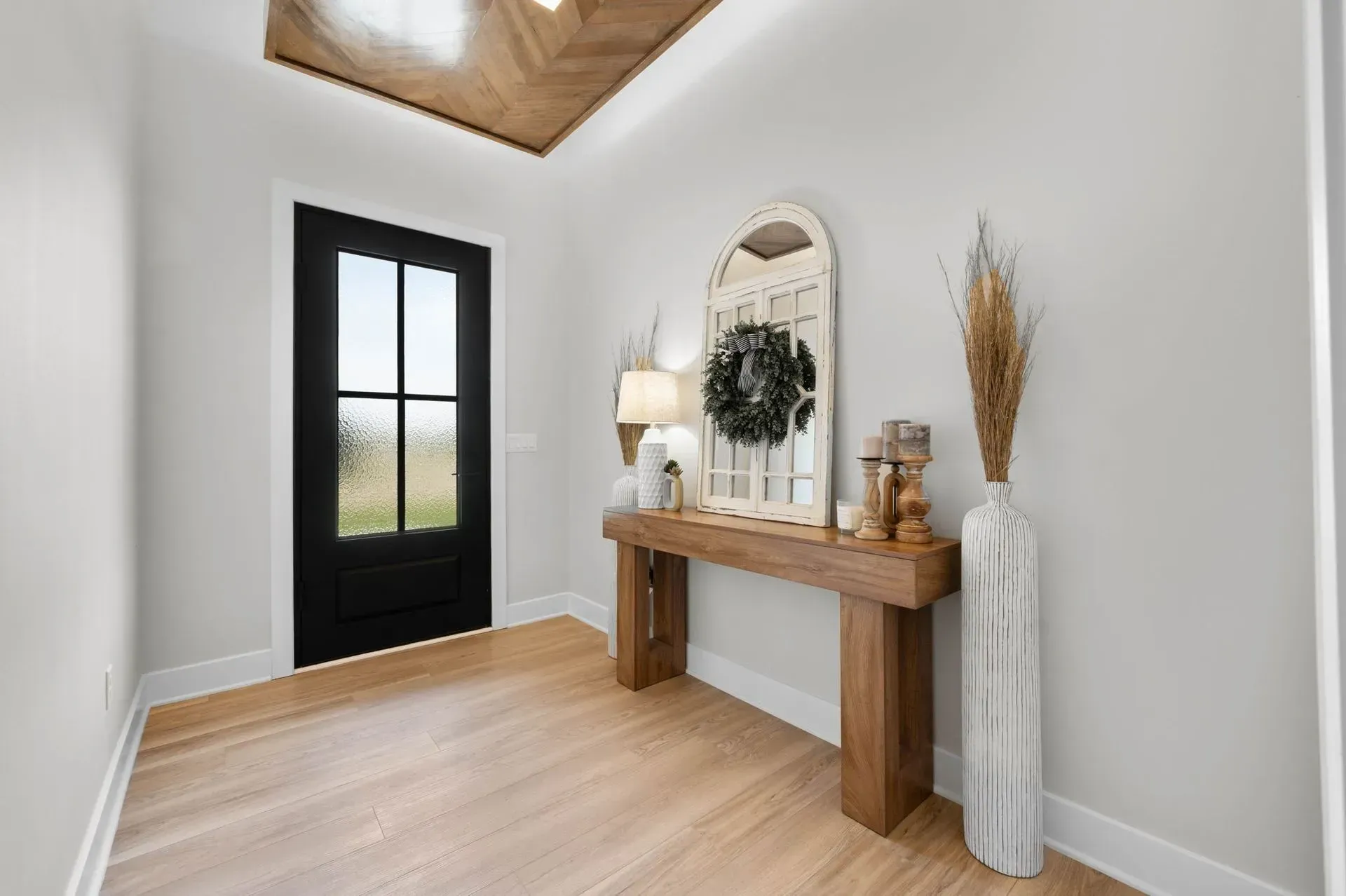 Bright entryway with black door, wood console table, arched mirror, and neutral decor on light wood floors.