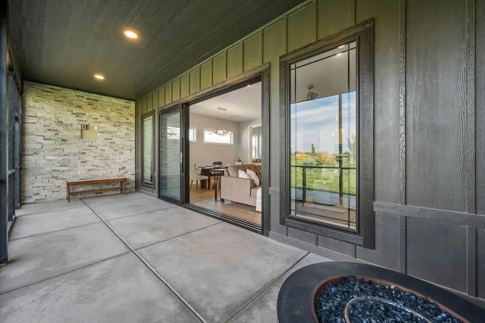 Covered patio with concrete floor, stone wall, and sliding glass doors opening to a dining room