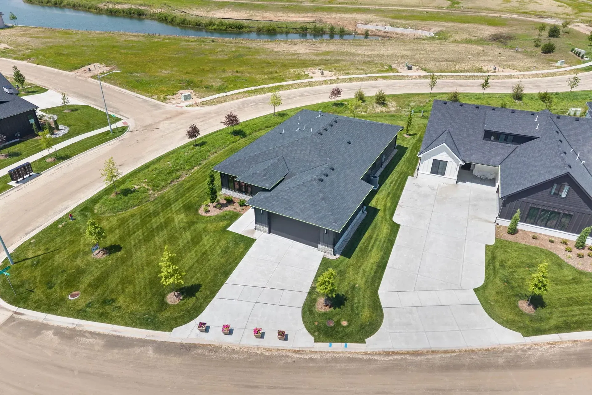 Aerial view of two modern houses with driveways and lawns beside a road and grassy drainage area.