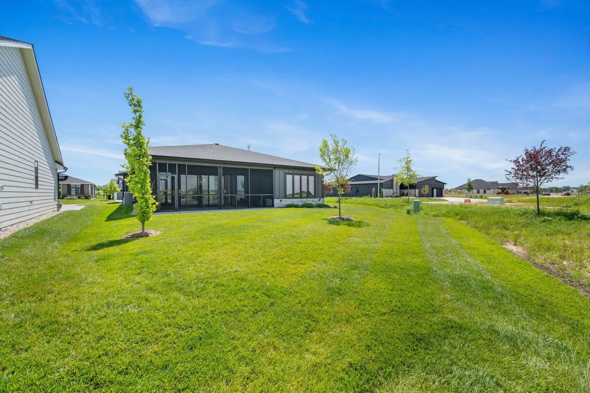 Modern single-story house with large green lawn under a bright blue sky