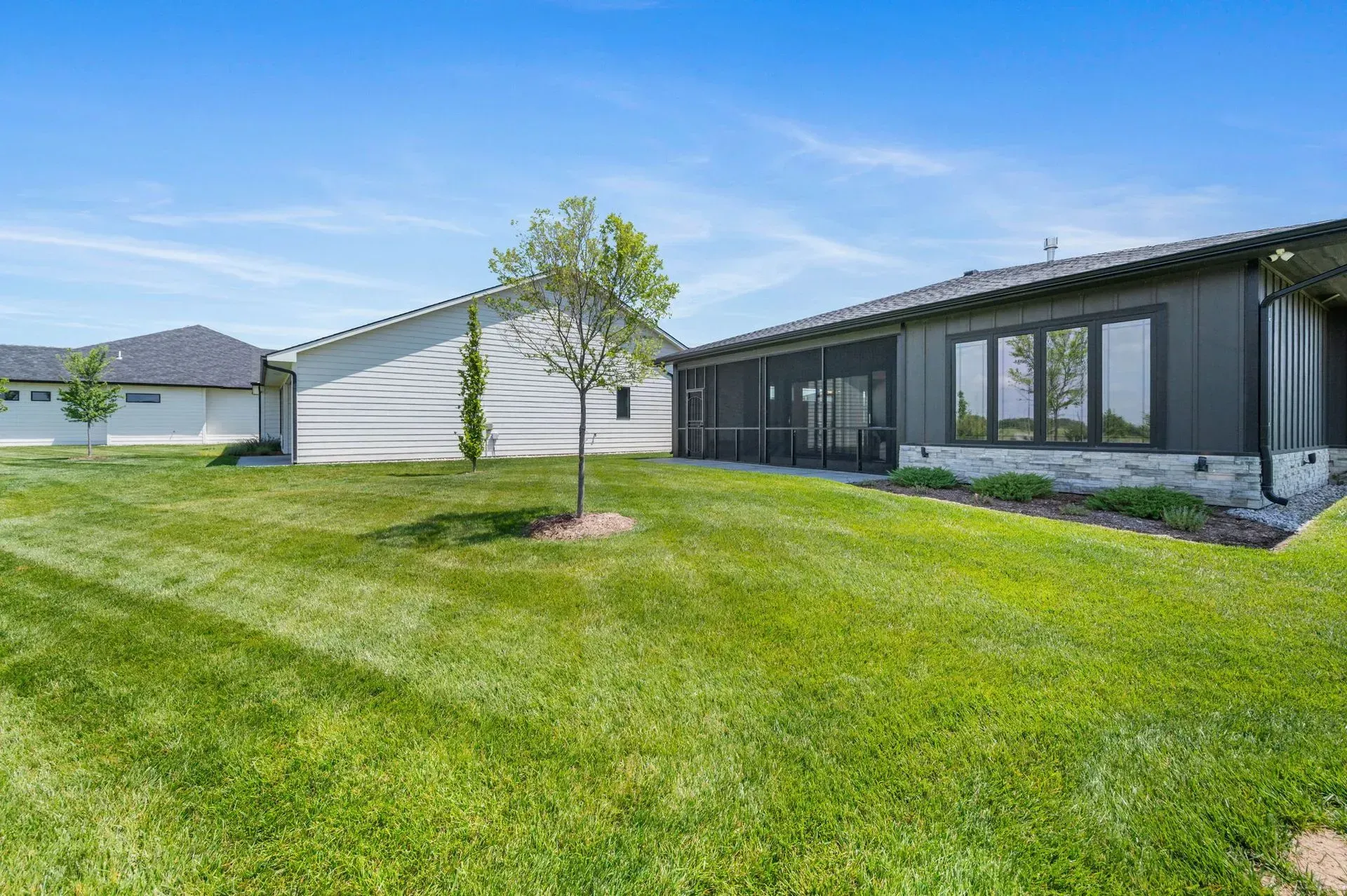 Modern single-story house with dark exterior and large green lawn under a bright blue sky