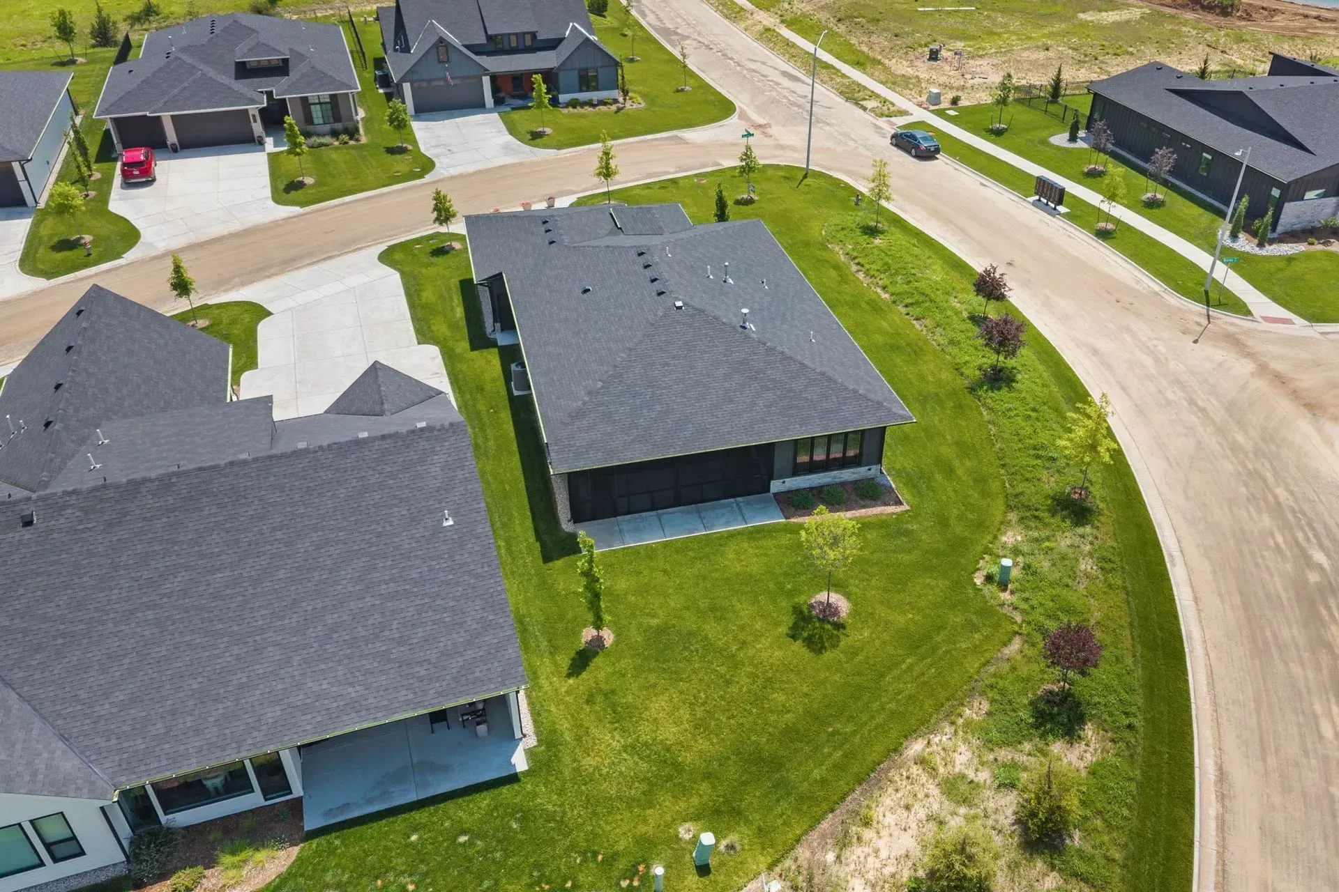 Aerial view of suburban houses with dark roofs, green lawns, and a curved street.