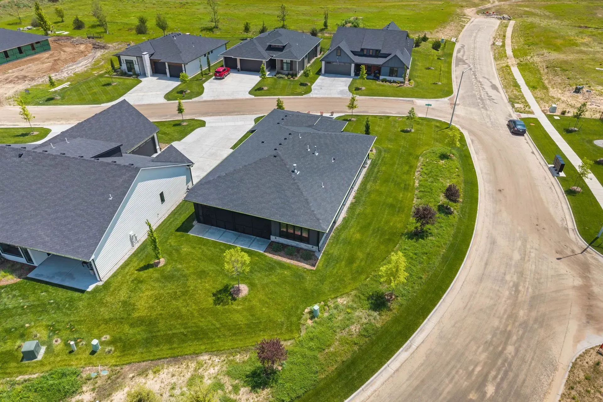 Aerial view of suburban homes with gray roofs along curving streets and green lawns