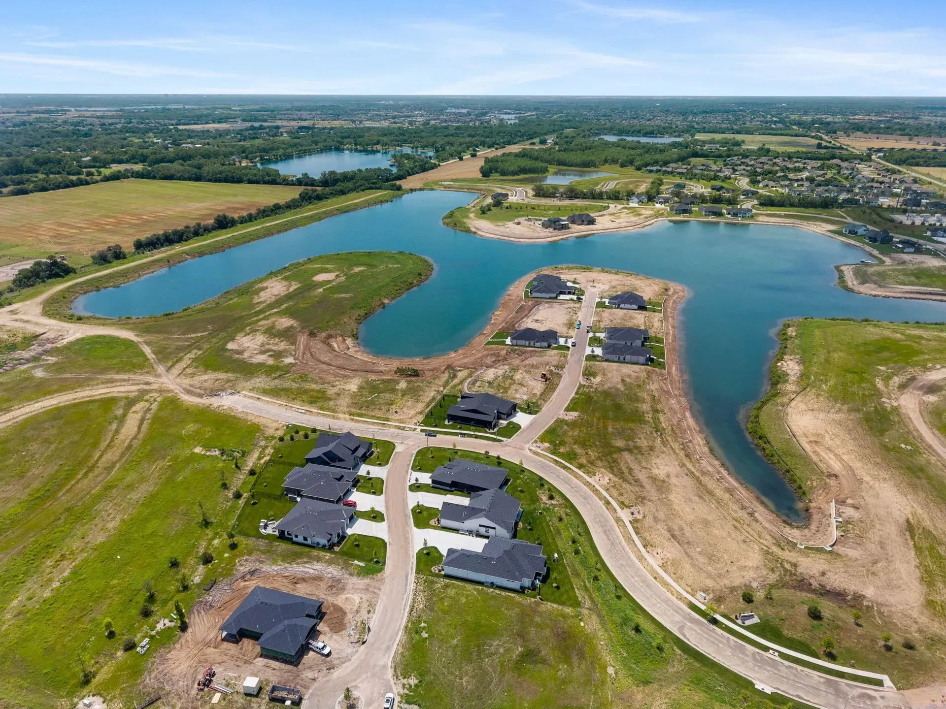 Aerial view of a lakeside neighborhood with houses, dirt roads, and blue water under a clear sky