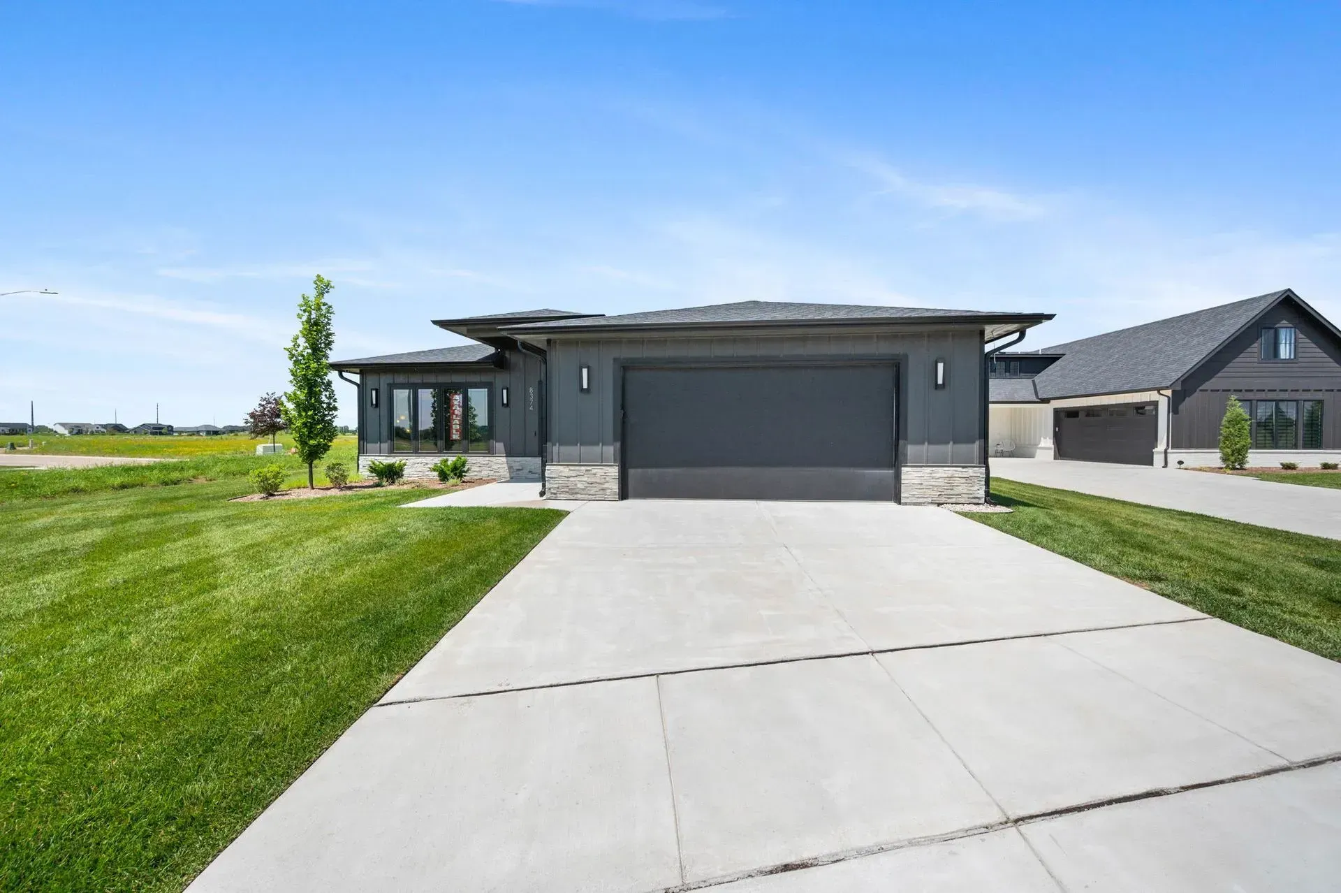 Modern single-story house with a gray garage, concrete driveway, and green lawn under a clear blue sky