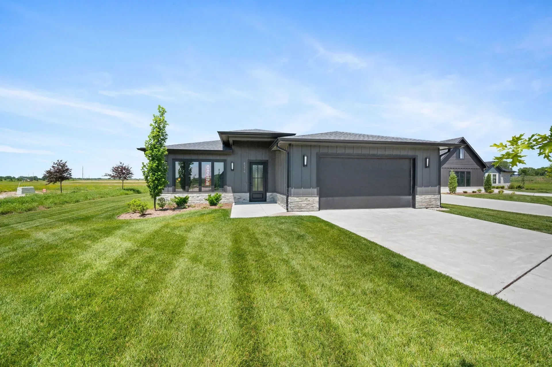 Modern single-story gray house with a large green lawn and concrete driveway under a clear blue sky