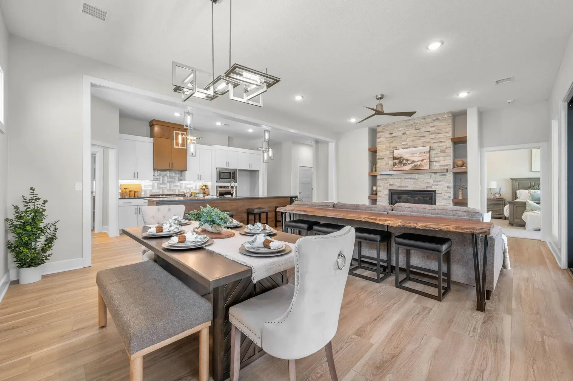 Modern open-concept kitchen and dining room with wood floors, dark table, white chairs, and stone fireplace.