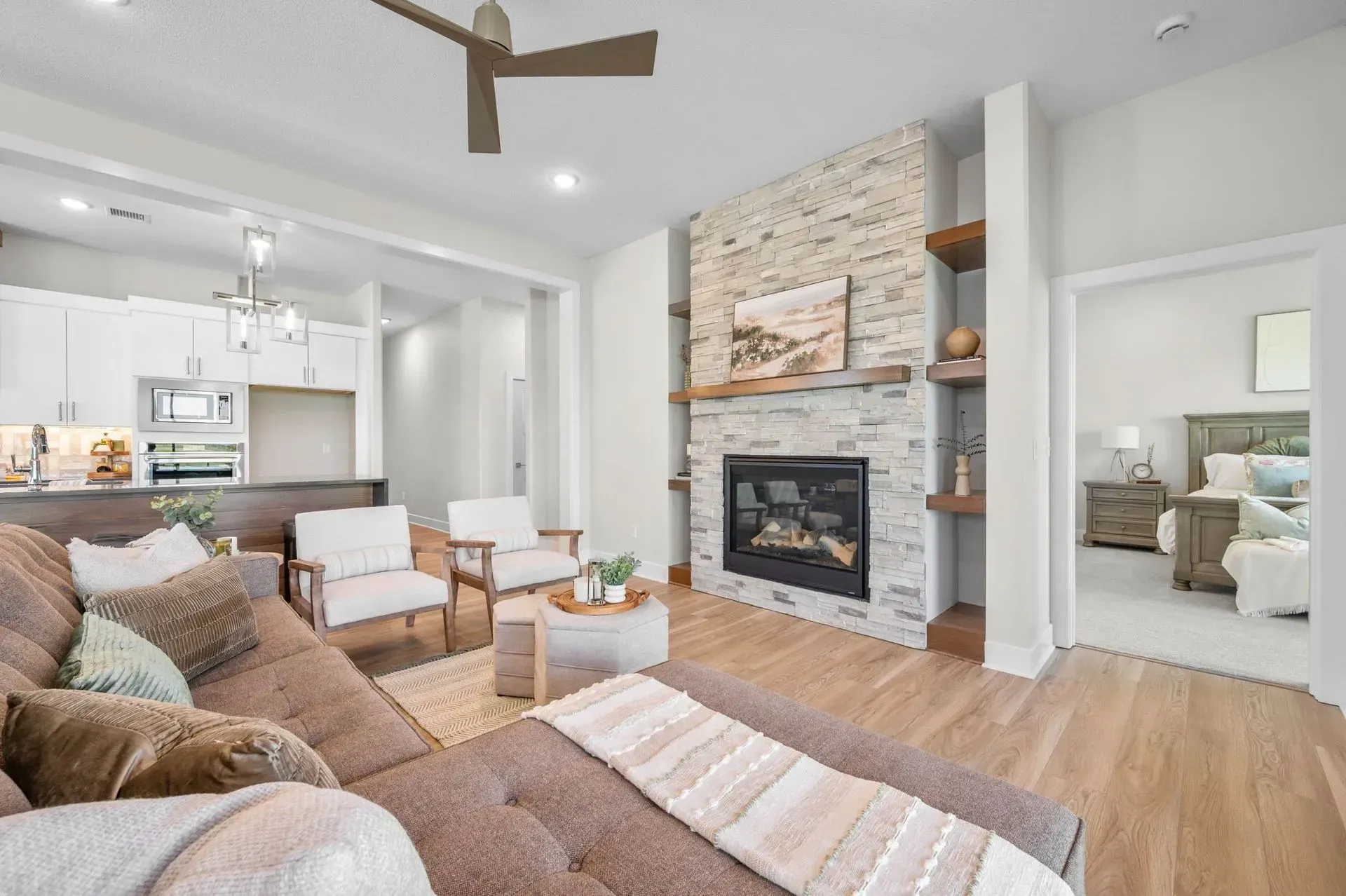 Bright open living room with stone fireplace, neutral sofa, wood floors, and adjoining kitchen
