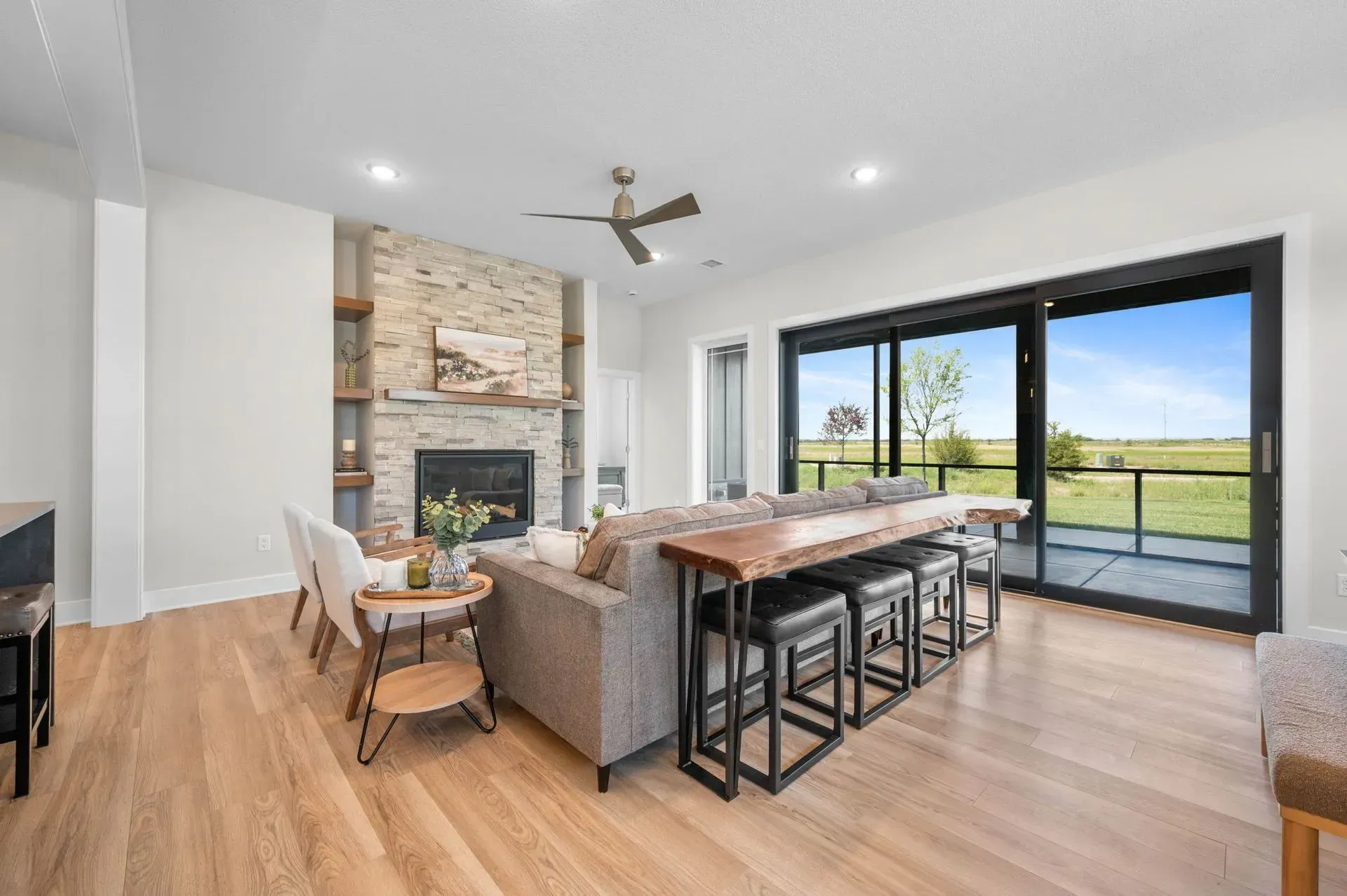 Bright modern living room with stone fireplace, wood floors, sectional, dining table, and large sliding glass doors