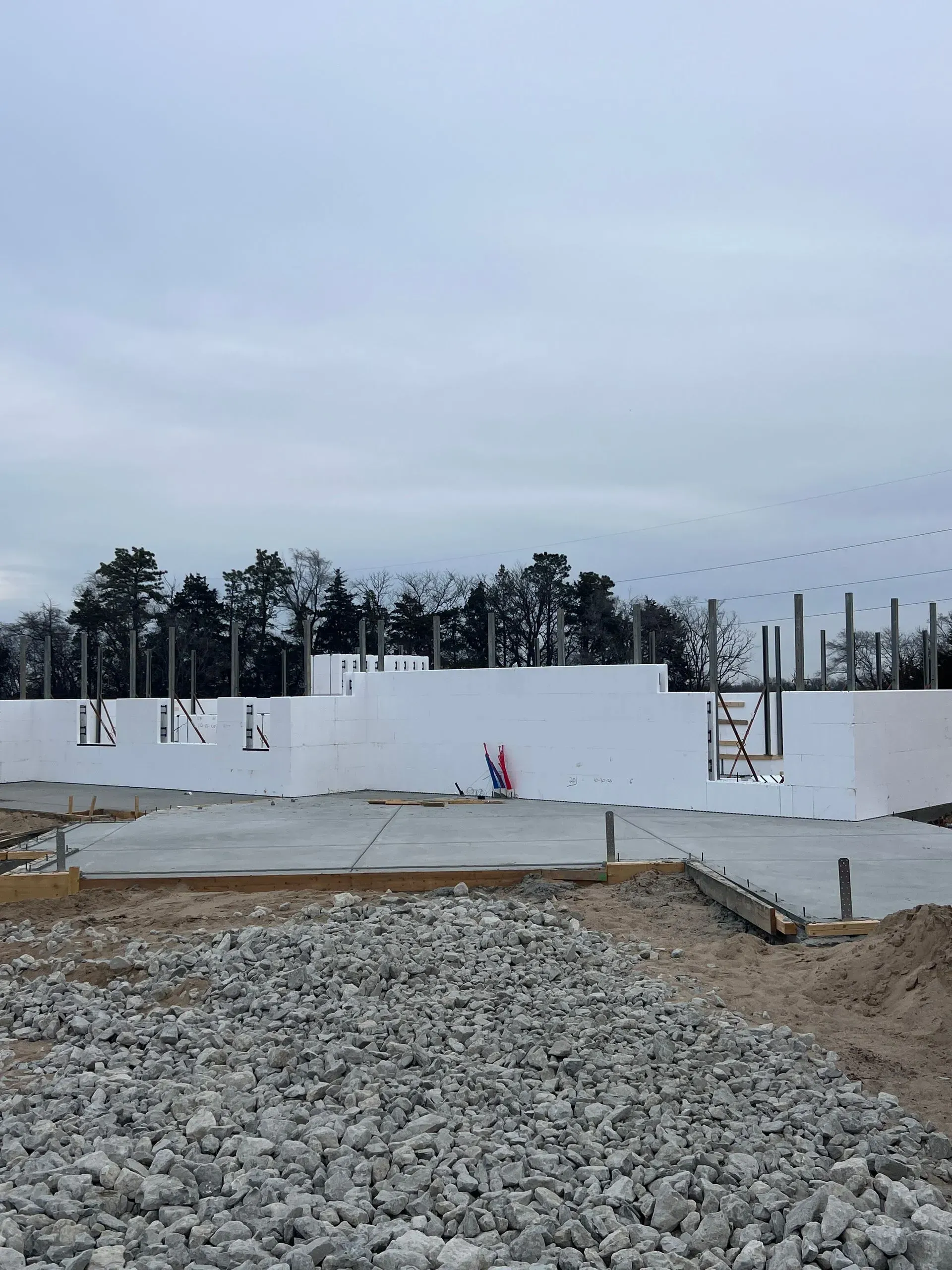 Partially built concrete foundation with gravel foreground and cloudy sky at a construction site
