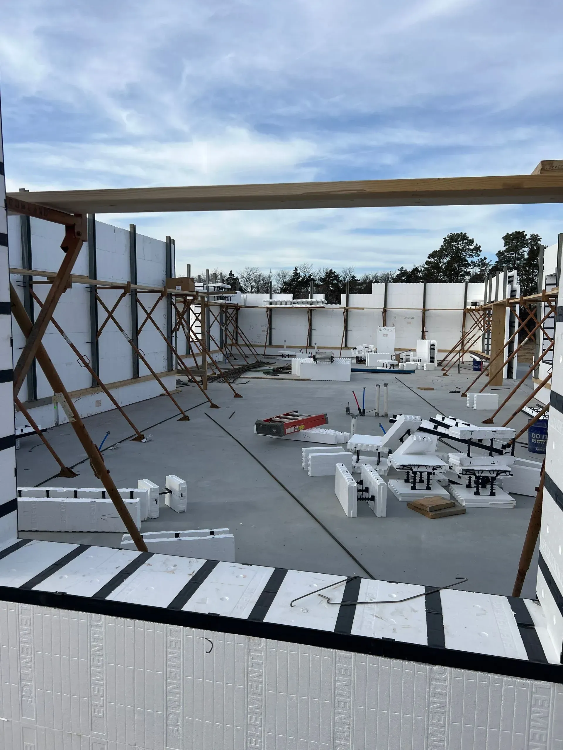 Rooftop construction site with white insulated walls, wooden framing, and scattered building materials under a cloudy sky