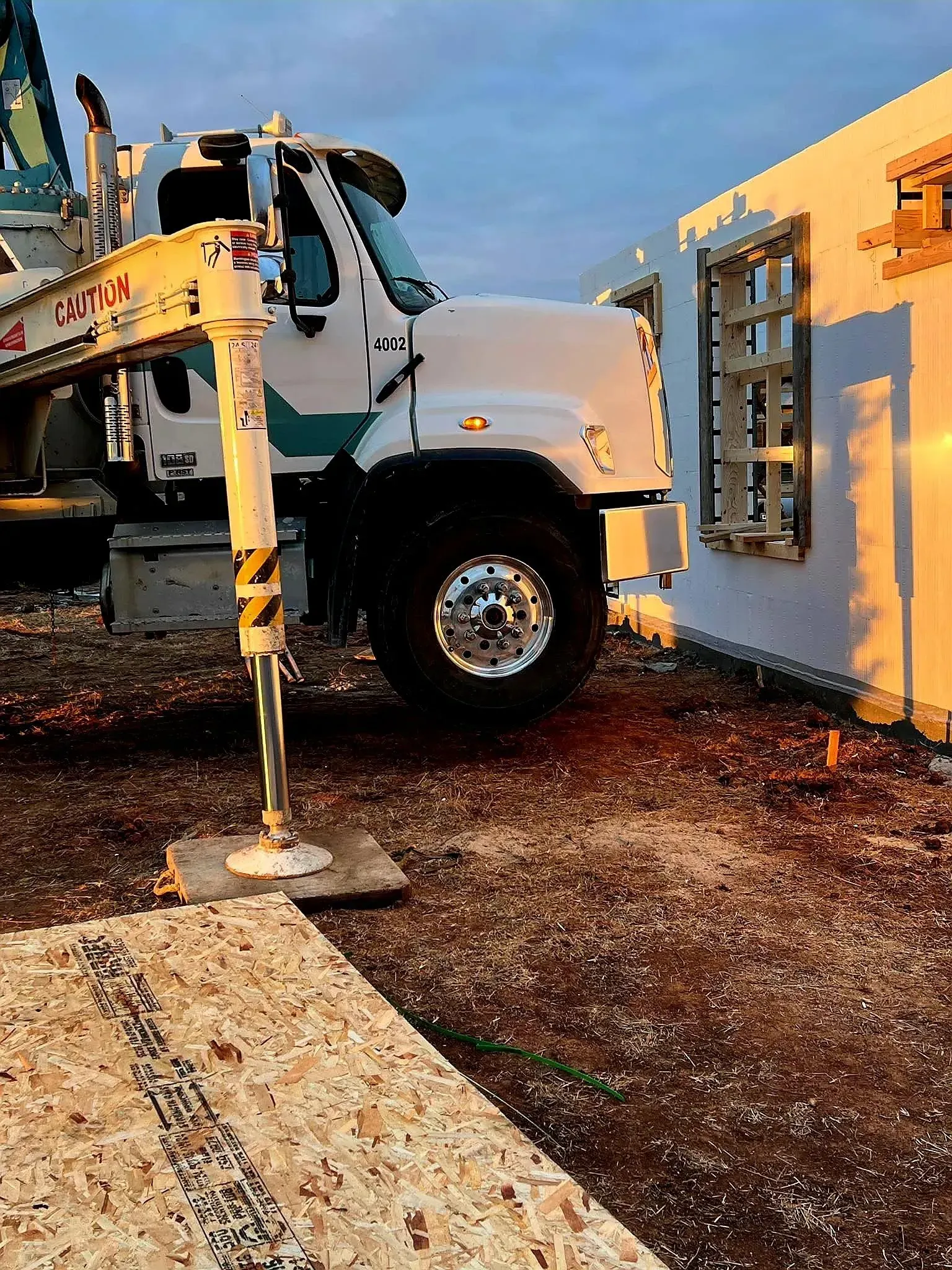 White utility truck parked beside a yellow building with a mounted ladder and work platform in the foreground
