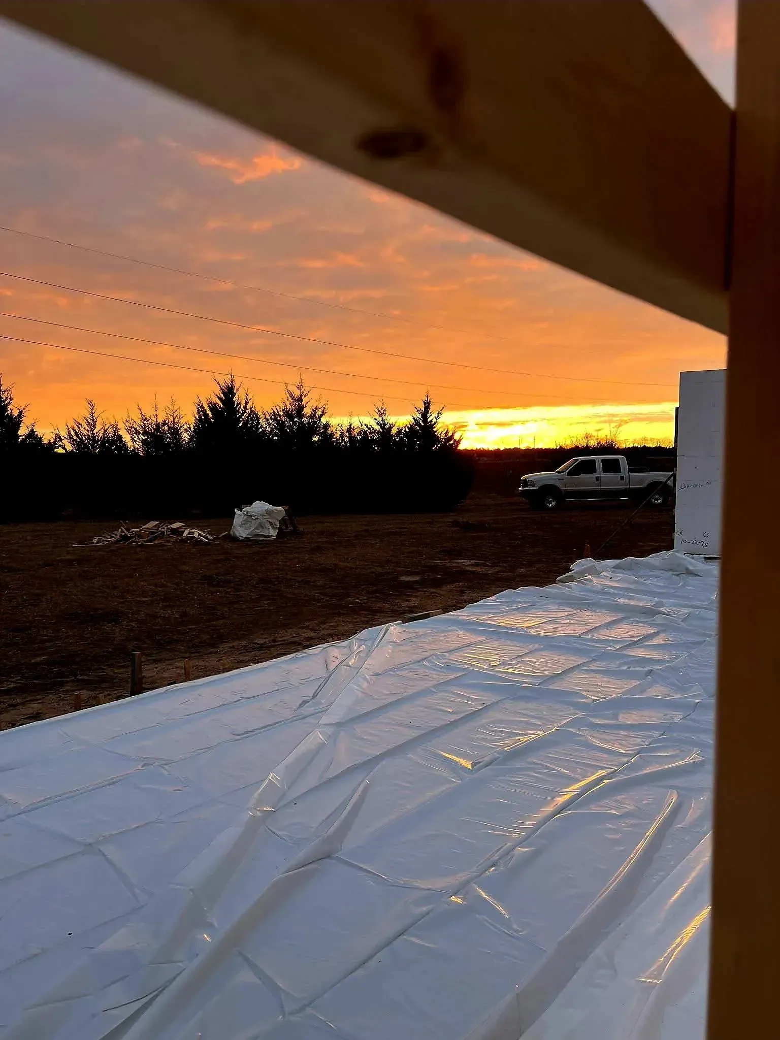 Sunset over snowy ground with orange sky, silhouetted trees, and a parked SUV near a building