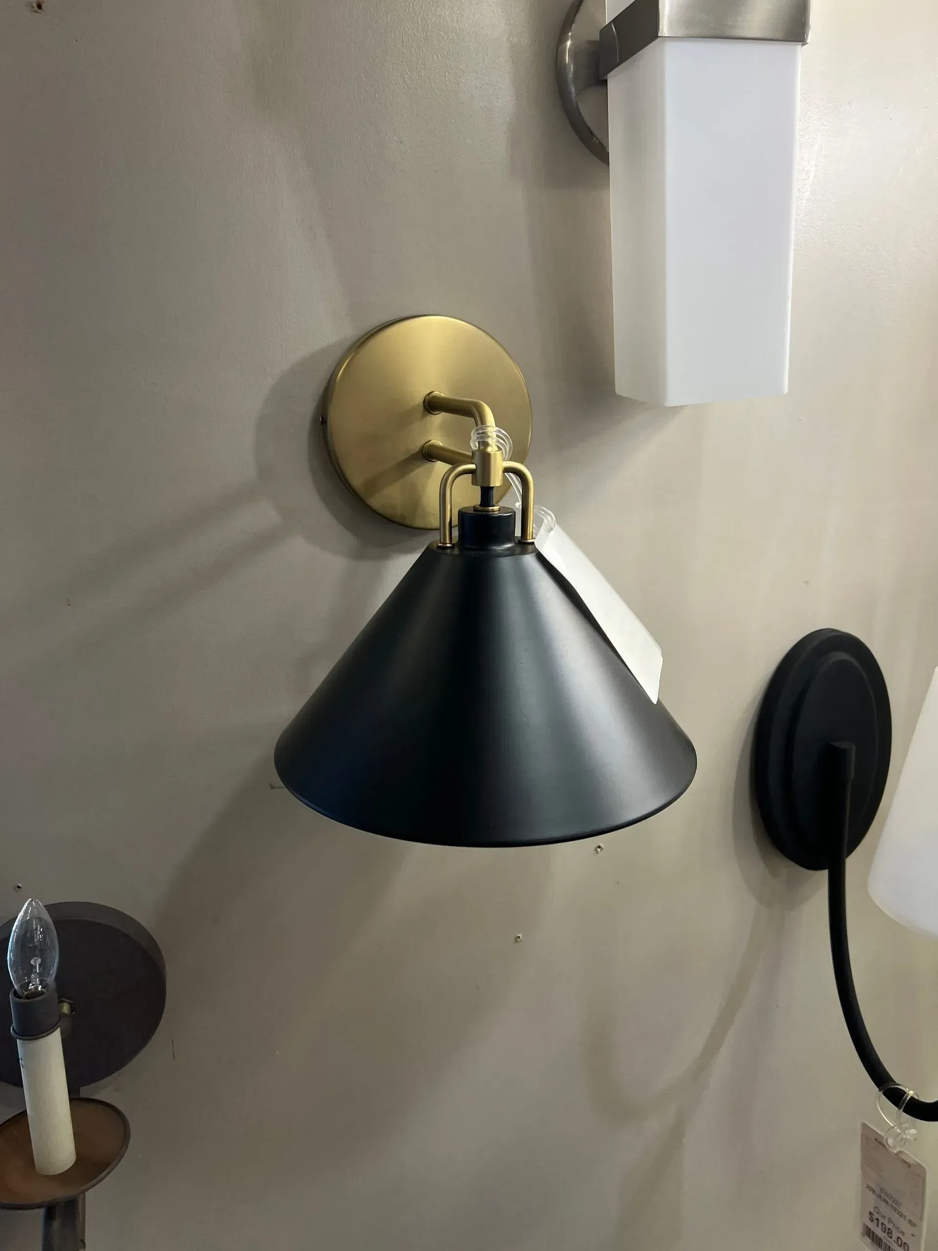 Brass wall sconce with black shade beside a wall-mounted white dispenser and black cable