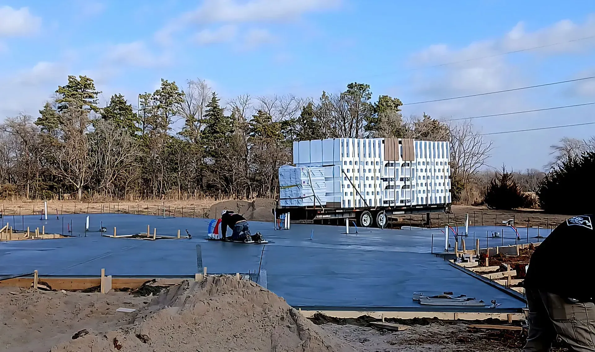 Concrete slab under construction with workers, rebar, and a large white modular building in the background