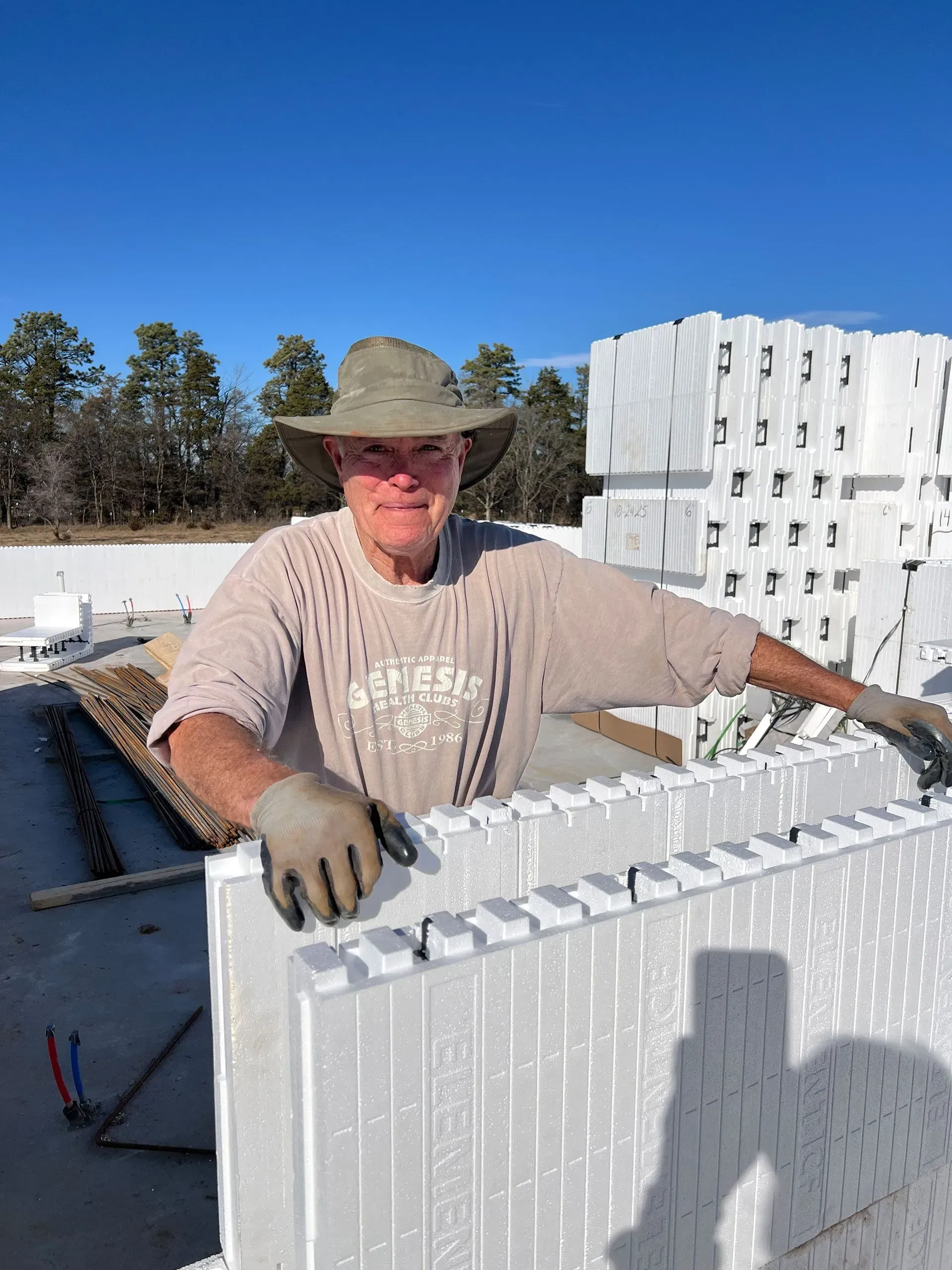Worker in sun hat and gloves standing beside stacked white foam blocks at a construction site under a blue sky